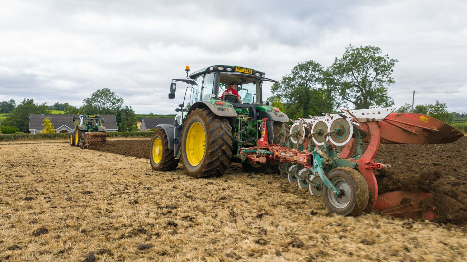 A line of farming tractors plowing fields in sequence during agricultural operations.
