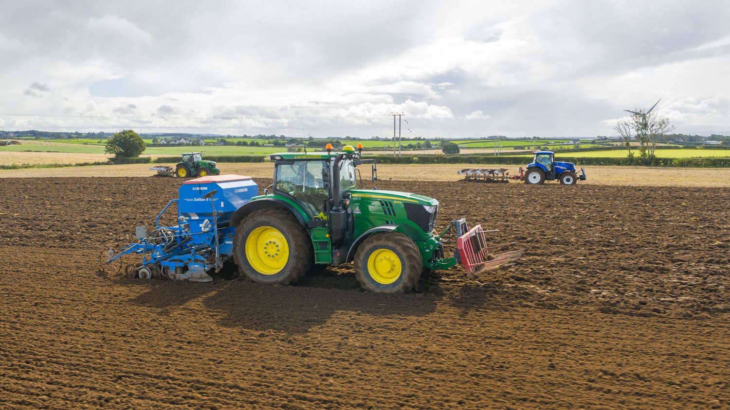 Panoramic view of tractor plowing farmland with agricultural machinery stretching across multiple fields.
