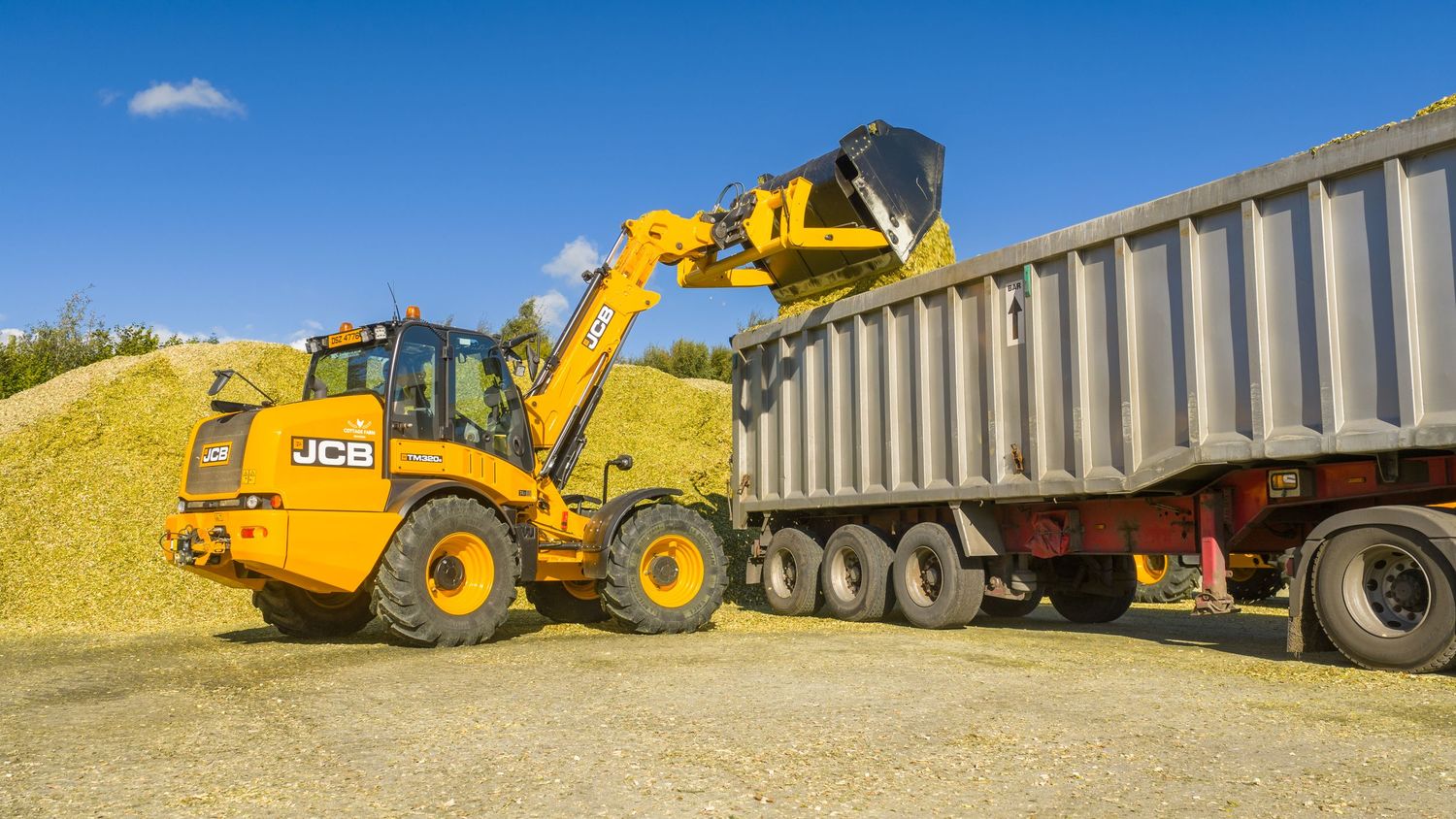 JCB backhoe loader dumps soil into a large dump truck during excavation work on a sunny day.
