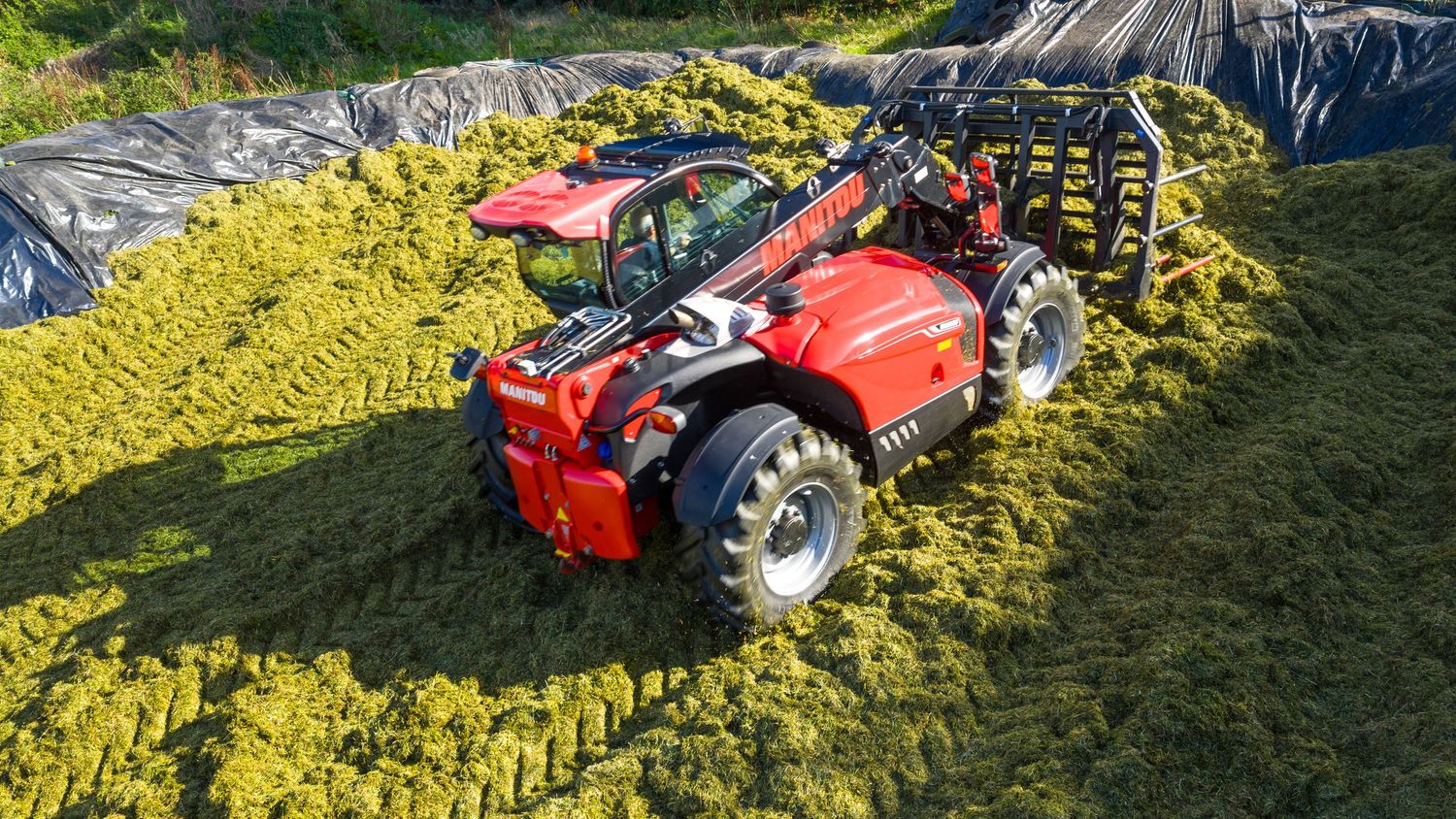 Agricultural machinery cutting and gathering hay in green field during summer harvest season.