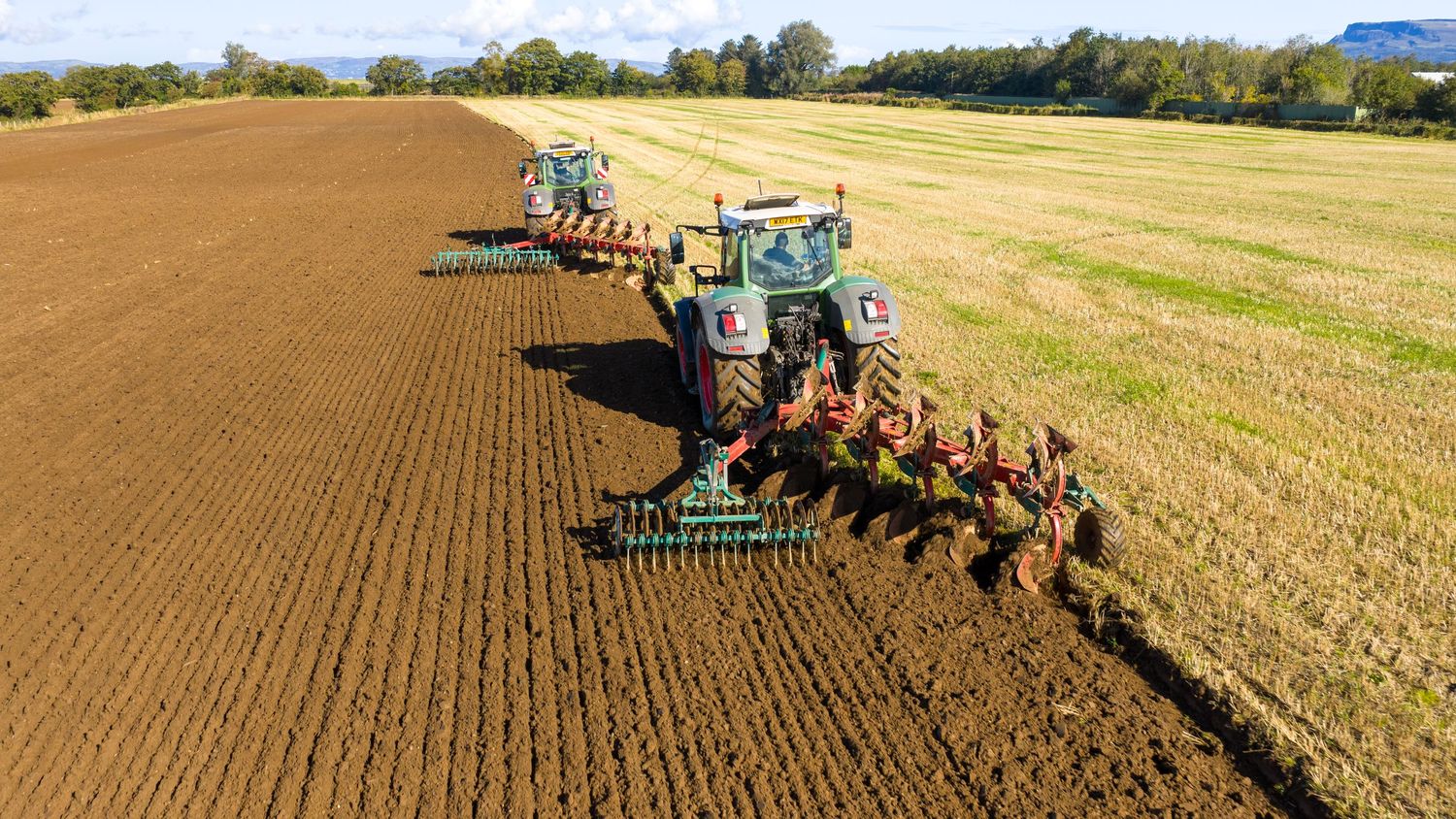 A panoramic view of agricultural machinery plowing and tilling farmland in a golden wheat field on a sunny day.