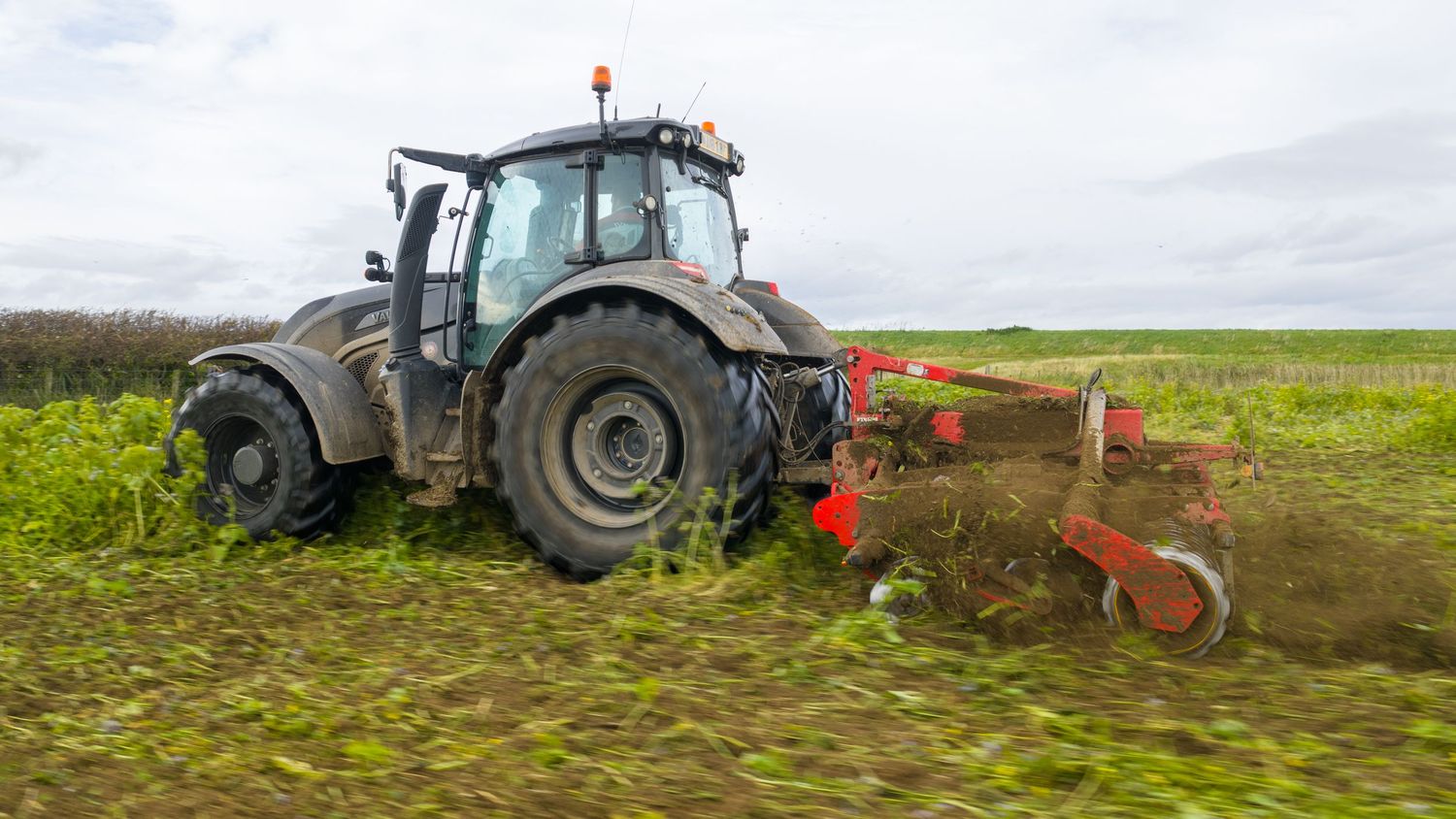 A tractor plows through agricultural fields during planting season on a cloudy day.