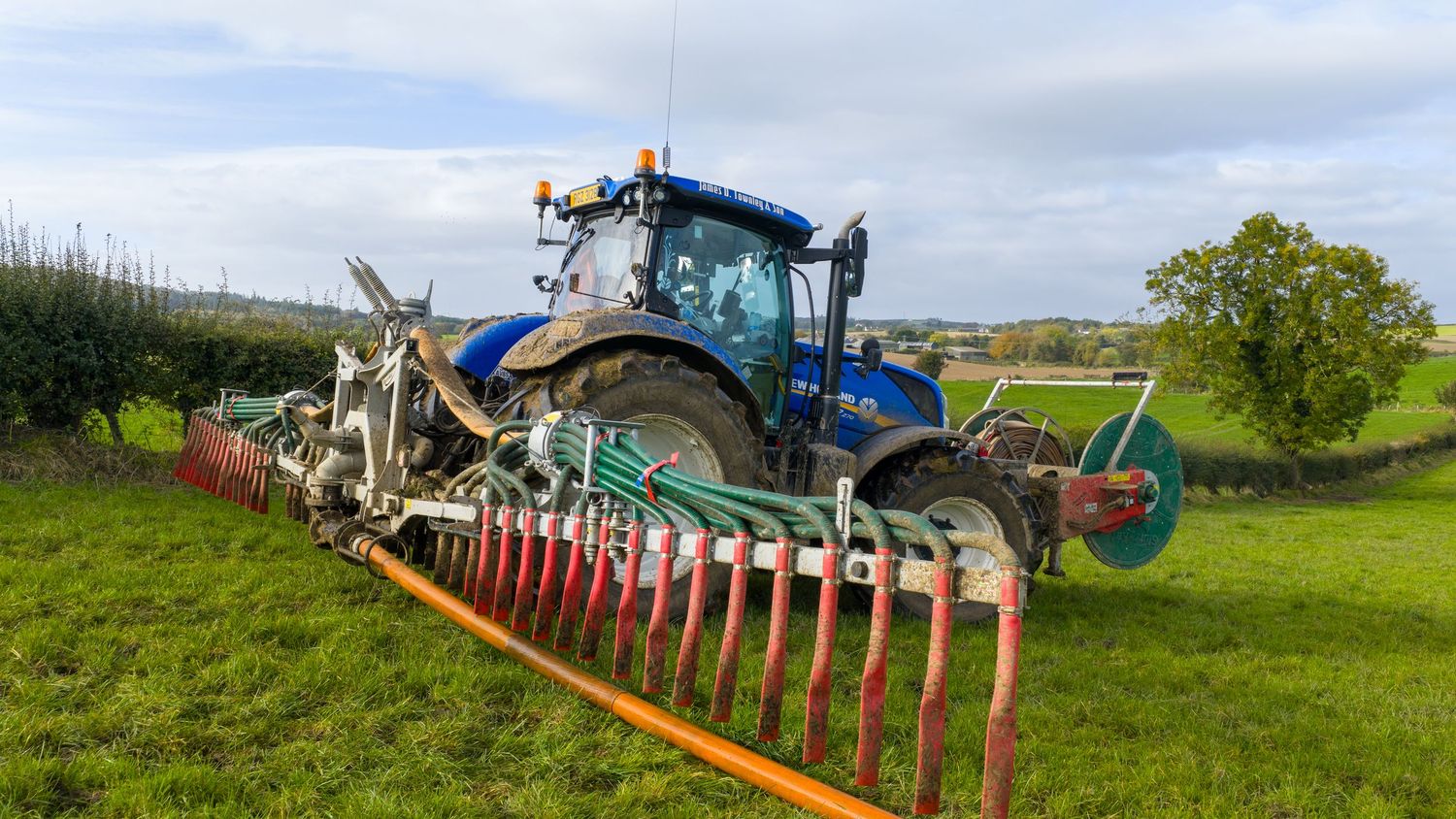 Panoramic view of agricultural machinery and equipment lined up in a green field with cloudy sky overhead.
