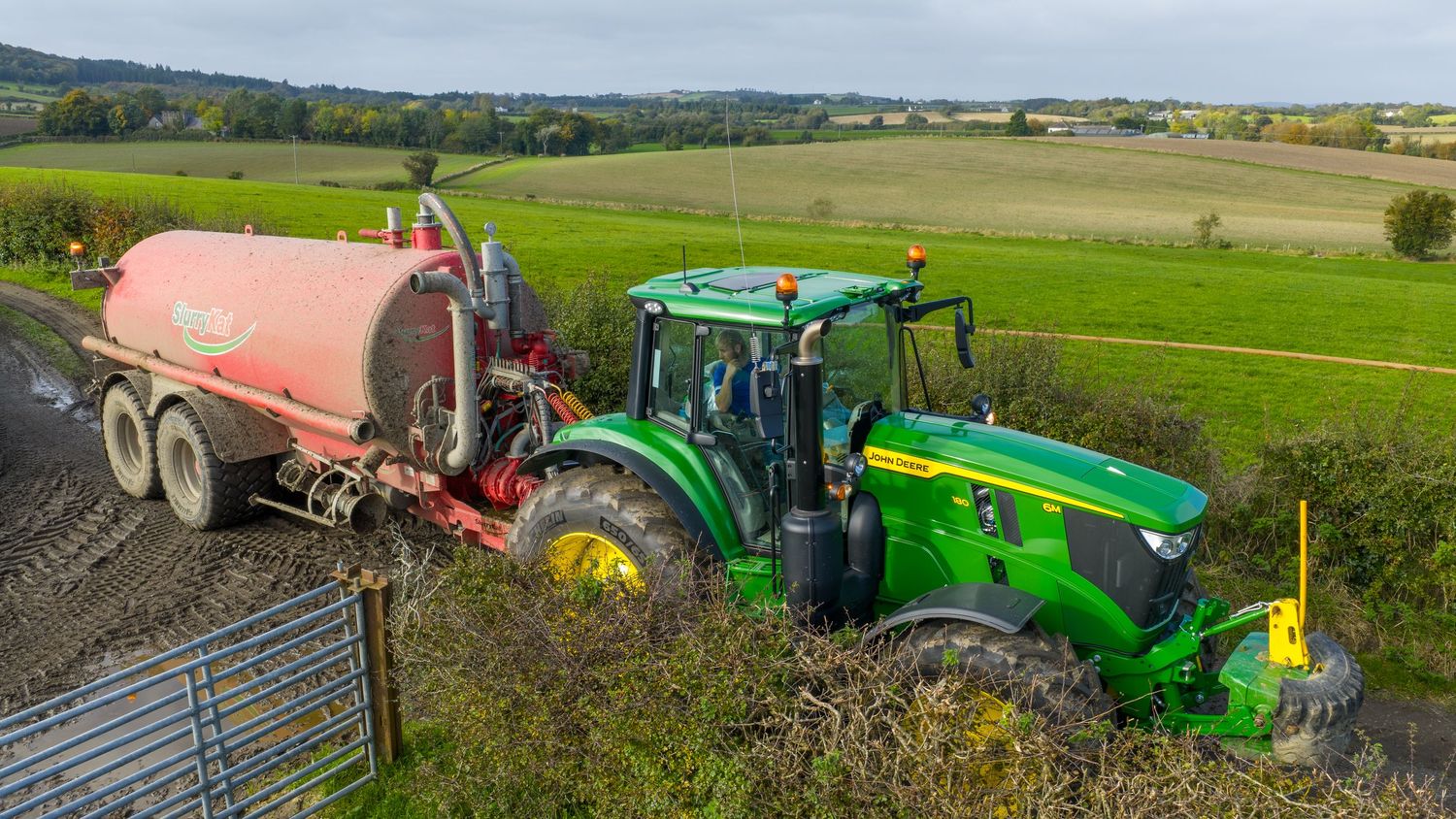 A panoramic view of agricultural fields with farm equipment and machinery working across green rolling landscapes.