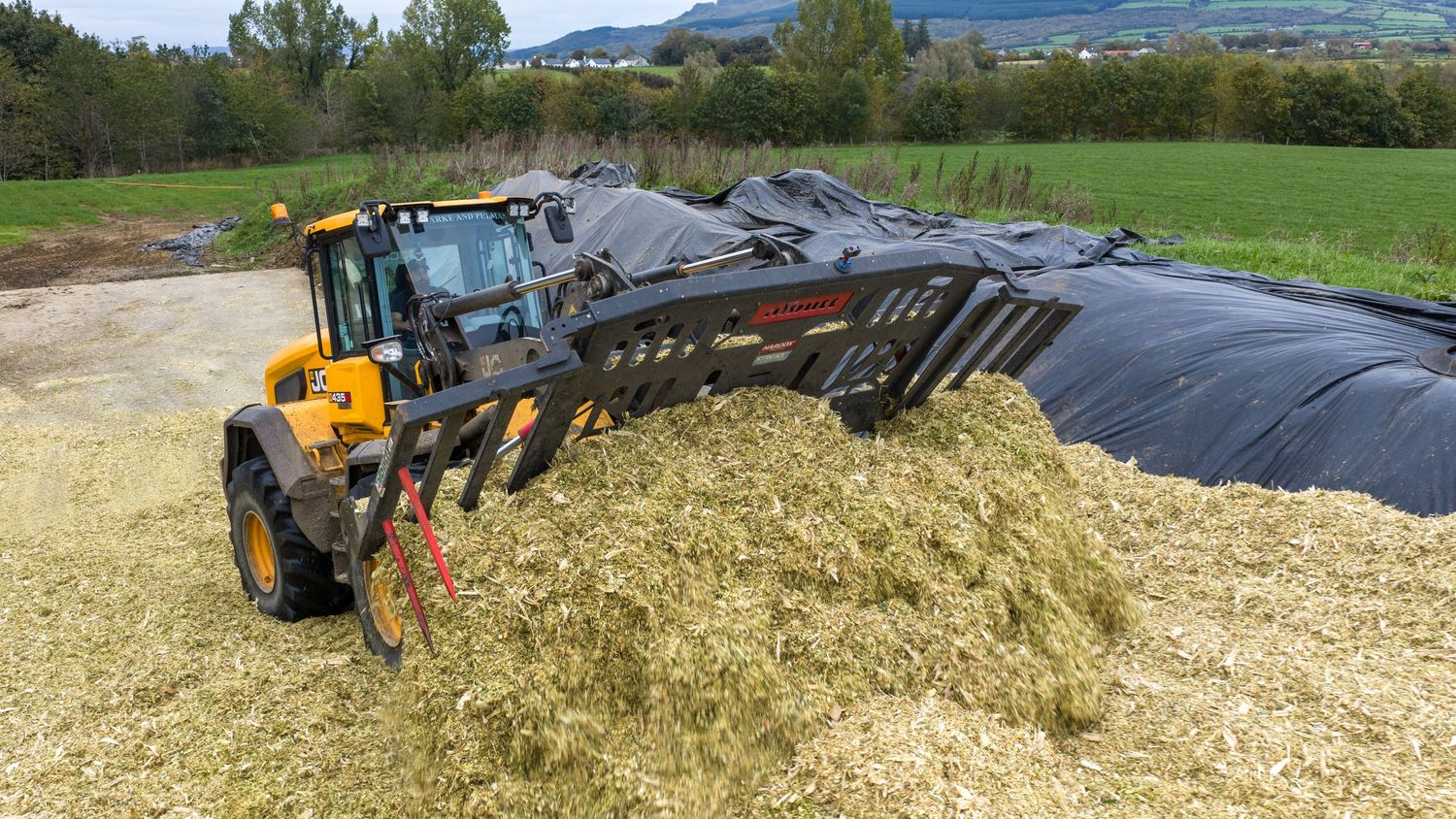 Heavy machinery spreads and compacts silage on a large farm bunker for livestock feed storage and preservation.