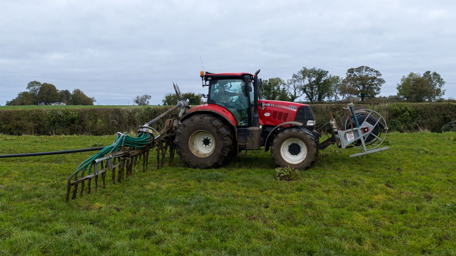 A red tractor pulling agricultural equipment across green farmland for soil preparation and cultivation.