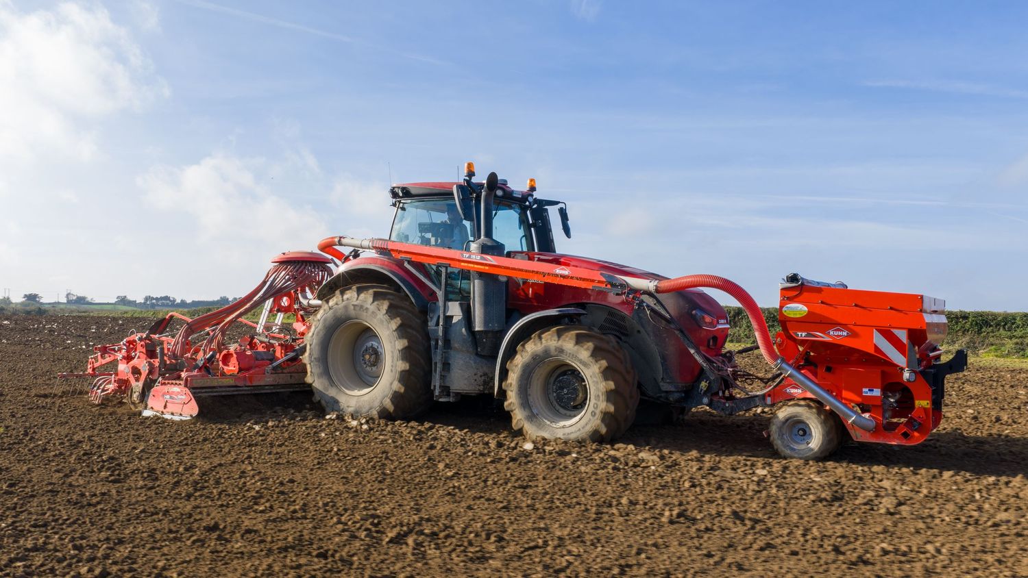 Panoramic view of agricultural tractors and machinery working in a field under blue skies during planting season.
