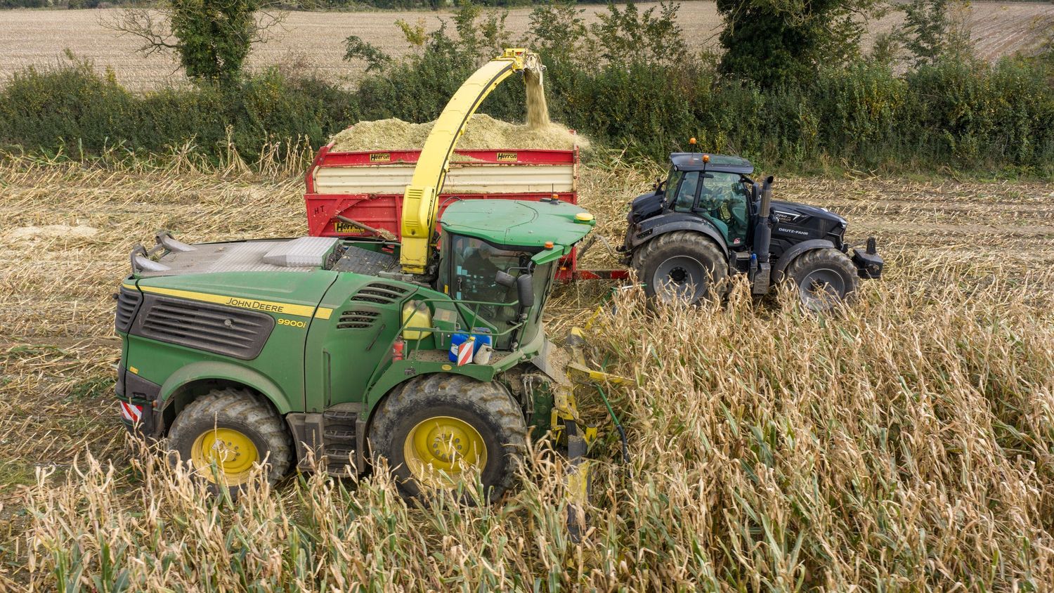 A tractor pulling farm equipment through a harvested cornfield at sunset creates a panoramic agricultural scene.