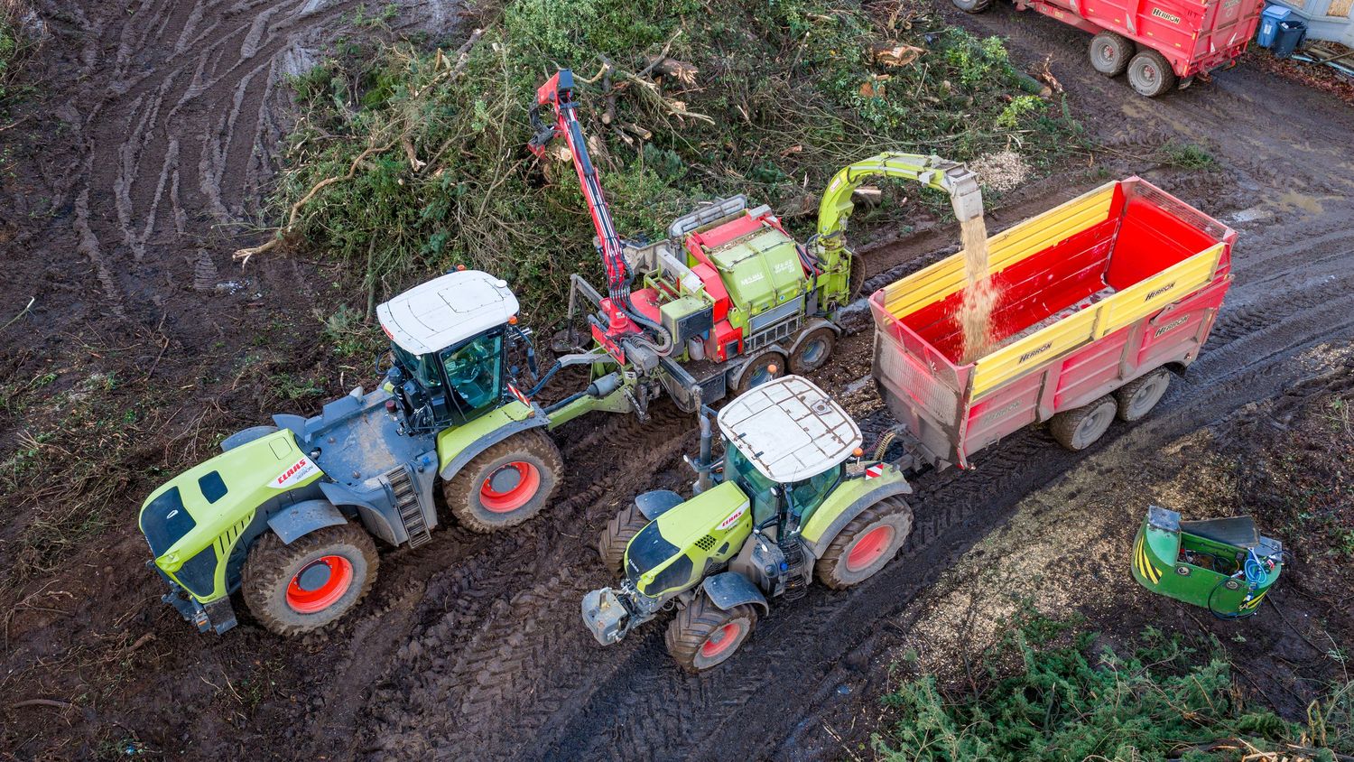 Aerial view of green tractors and red farm equipment working together in muddy field conditions.