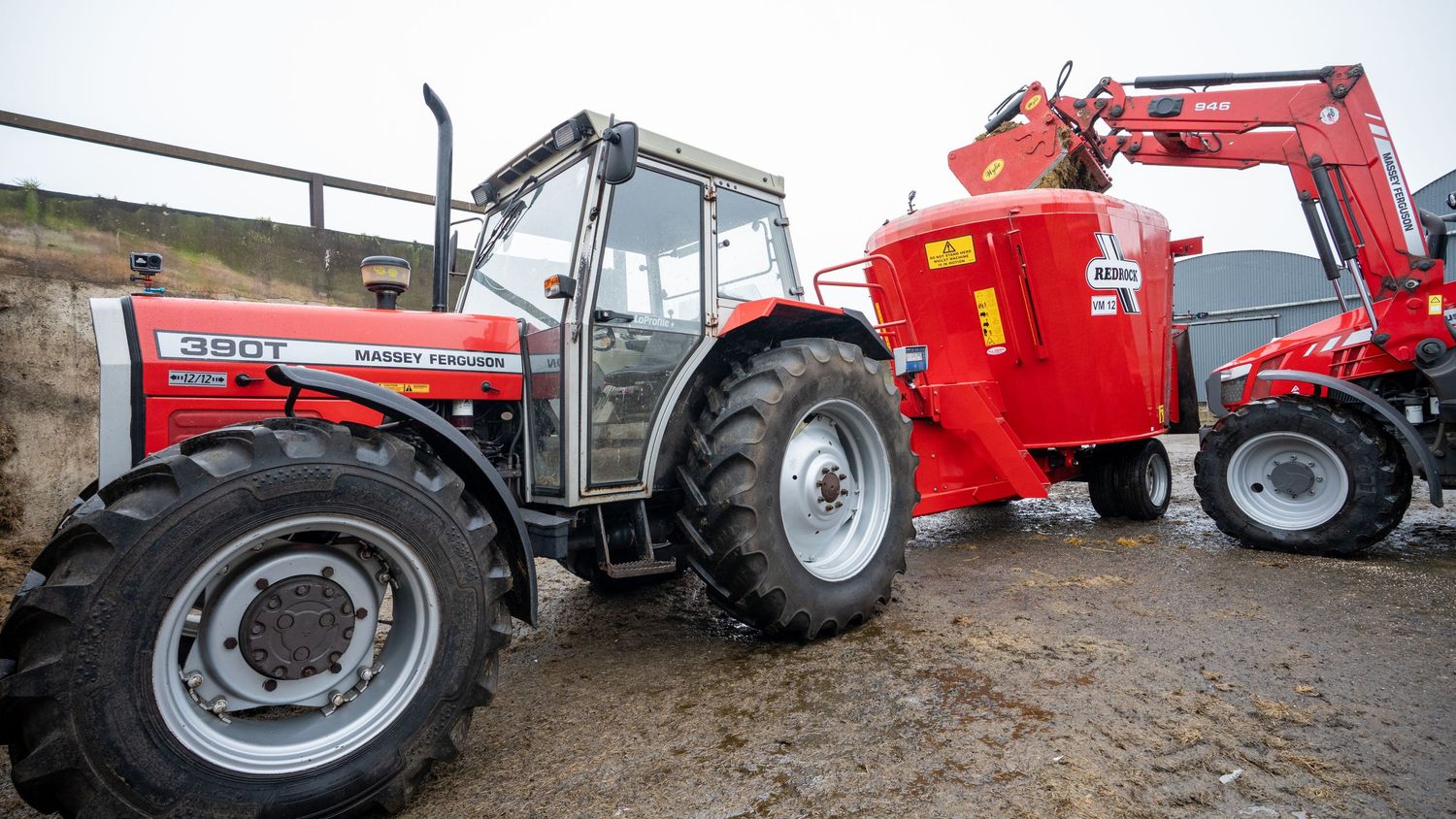 Massey Ferguson red tractor parked next to farm machinery equipment in rural agricultural setting.