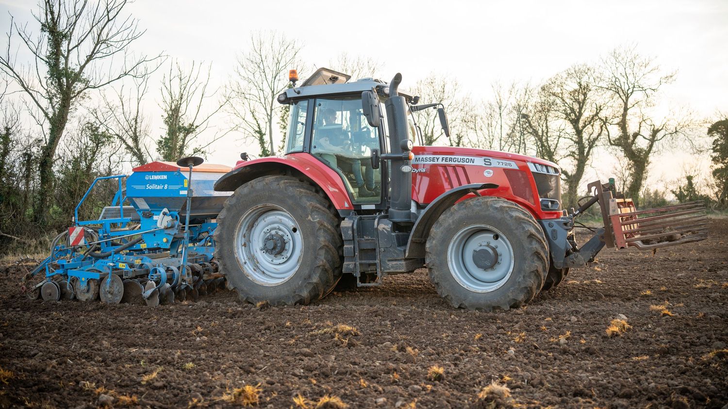 Red Massey Ferguson tractor with blue agricultural equipment working in a muddy field during late autumn.