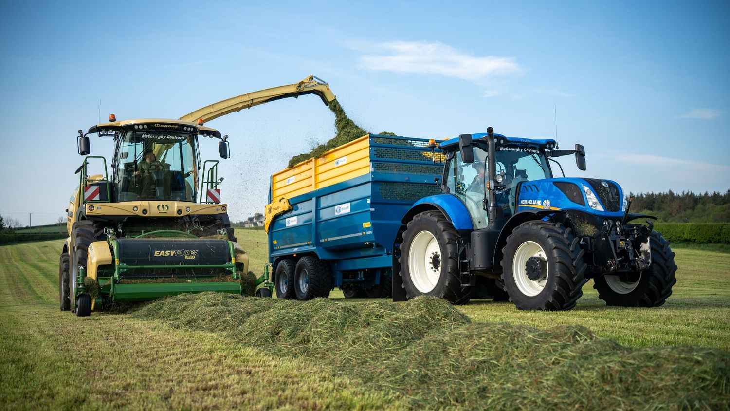 Modern combine harvester and tractor work together to collect silage in rural farmland setting.