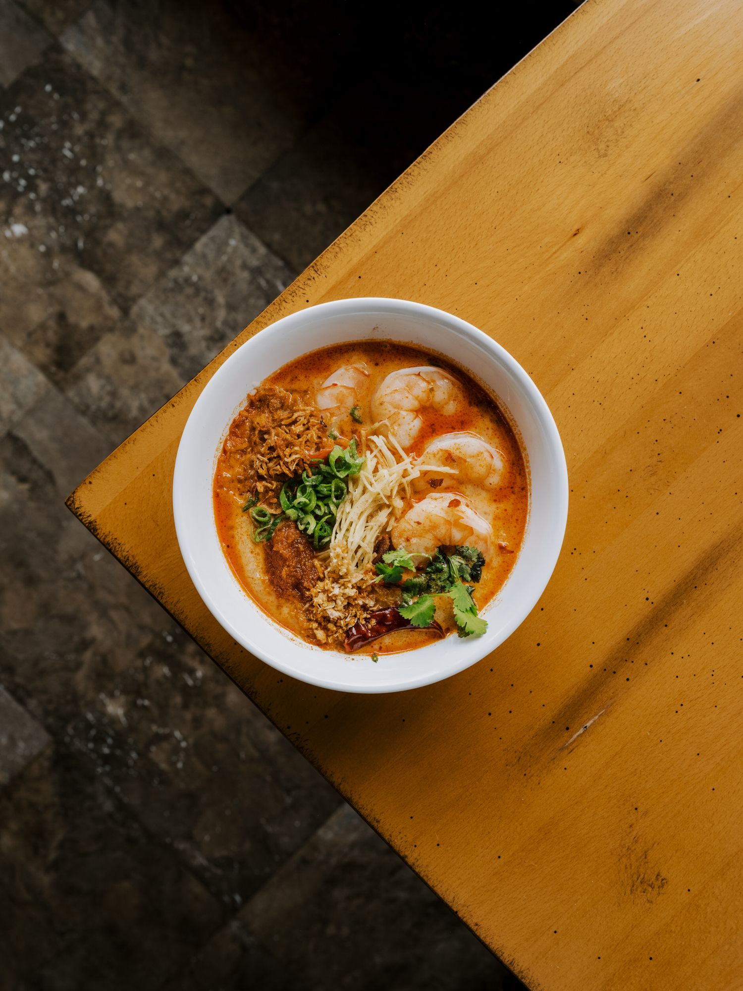 Spicy Asian soup bowl with shrimp dumplings garnished with green onions and chili oil.