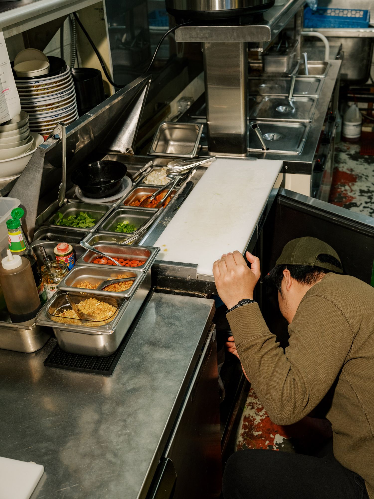 Commercial kitchen worker preparing food at stainless steel prep station with organized ingredient containers.