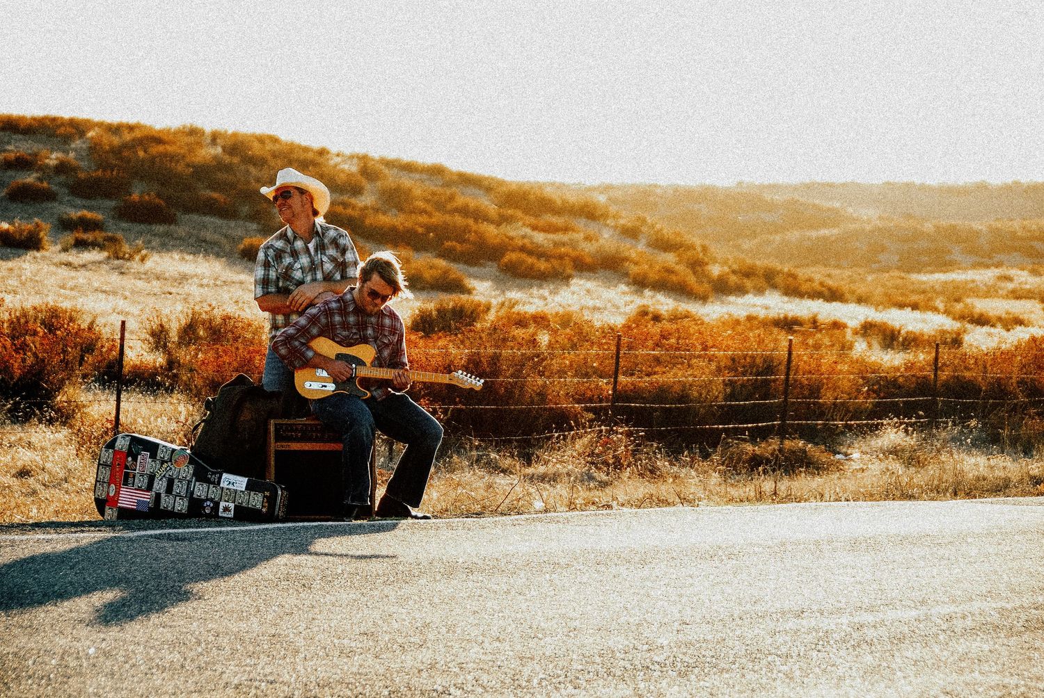Person sitting outdoors on a skateboard during golden hour on an empty road in autumn landscape.
