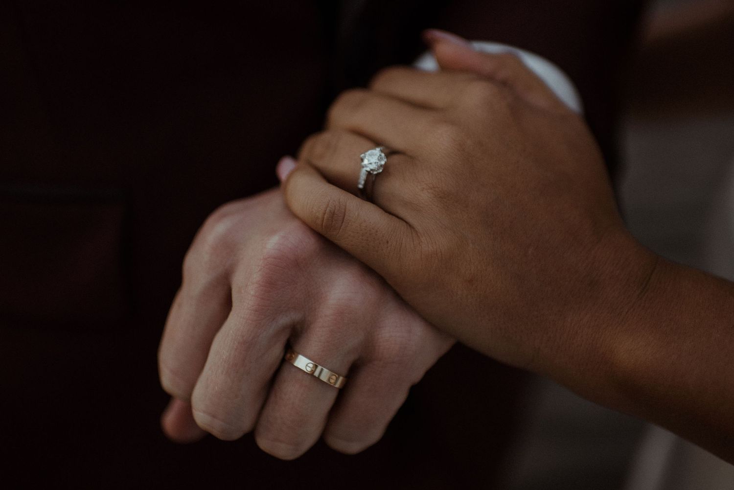 Close-up shot of two hands wearing wedding rings against a dark background in intimate lighting.