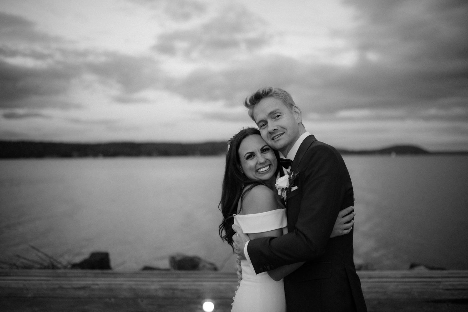 Newlywed couple embraces against a moody waterfront backdrop during sunset at Villa Malla in Filtvet, Norway.