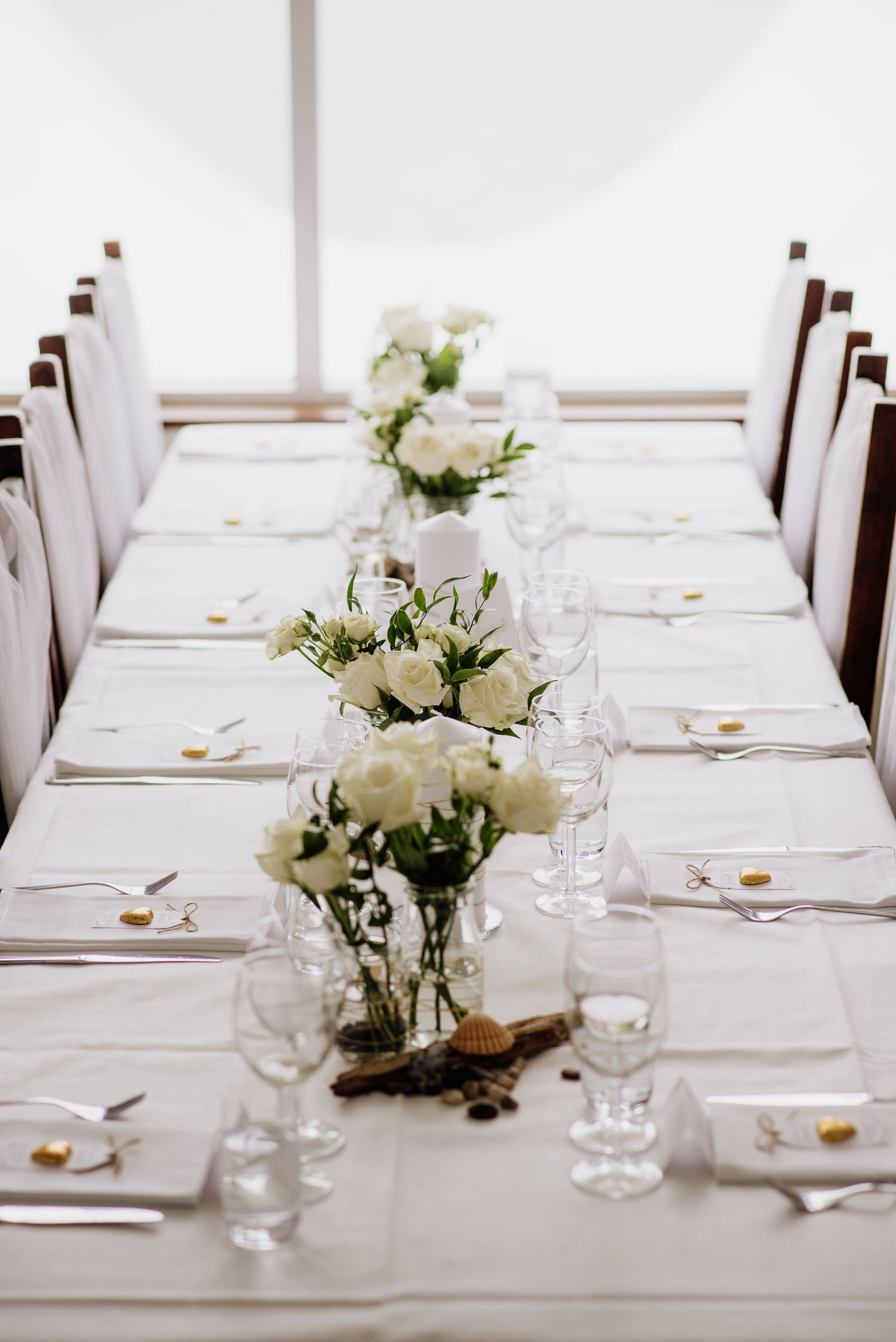 Elegant wedding table setting with white flowers in glass vases, white linens, and rustic accents running down the center at Villa Malla,
