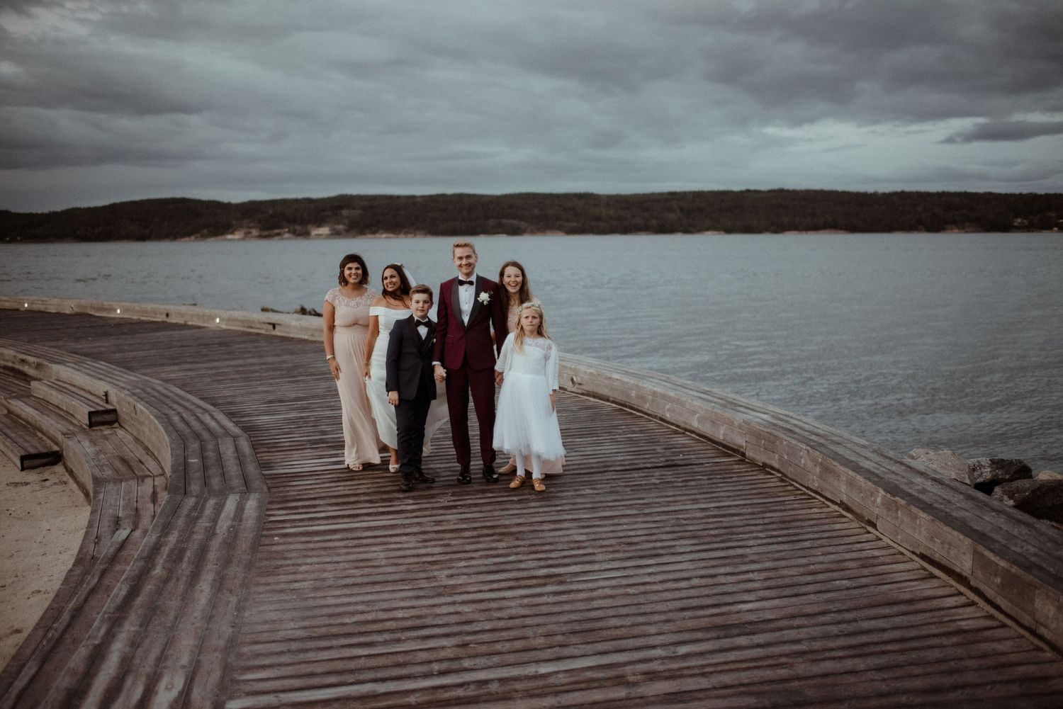 Wedding party poses together on a wooden boardwalk by a serene fjord at Villa Malla in Filtvet, Norway..