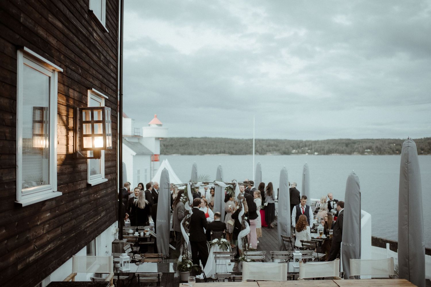 Wedding guests gather on an outdoor deck overlooking a waterfront view under cloudy skies Villa Malla in Filtvet, Norway.