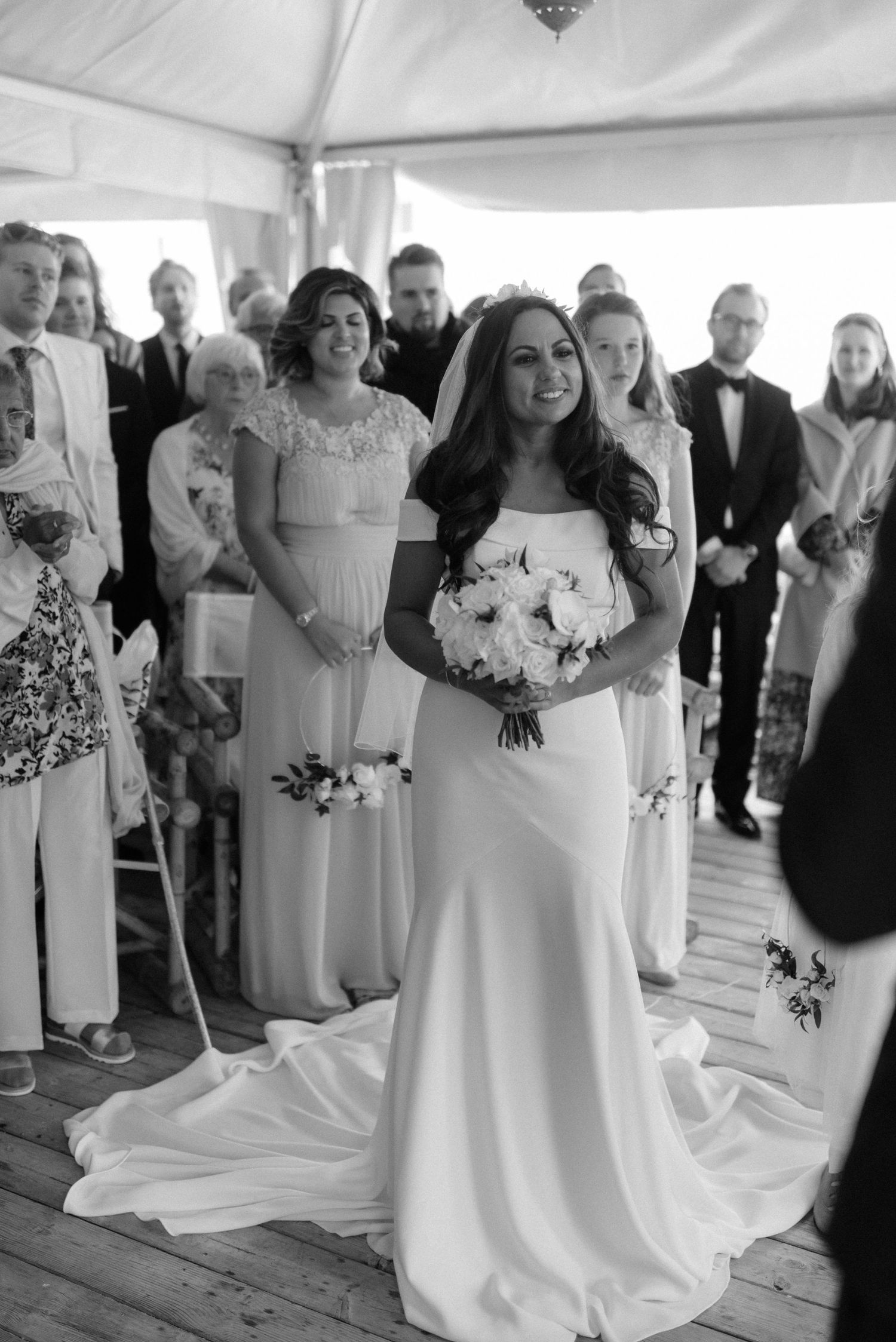 Black and white photo of elegant wedding party gathered under a tent with bride in flowing white gown holding bouquet at Villa Malla.