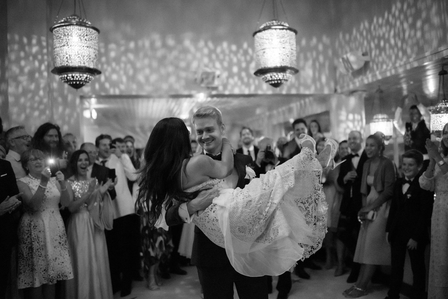 A black and white photo captures a romantic moment on a dance floor surrounded by guests at an elegant reception.