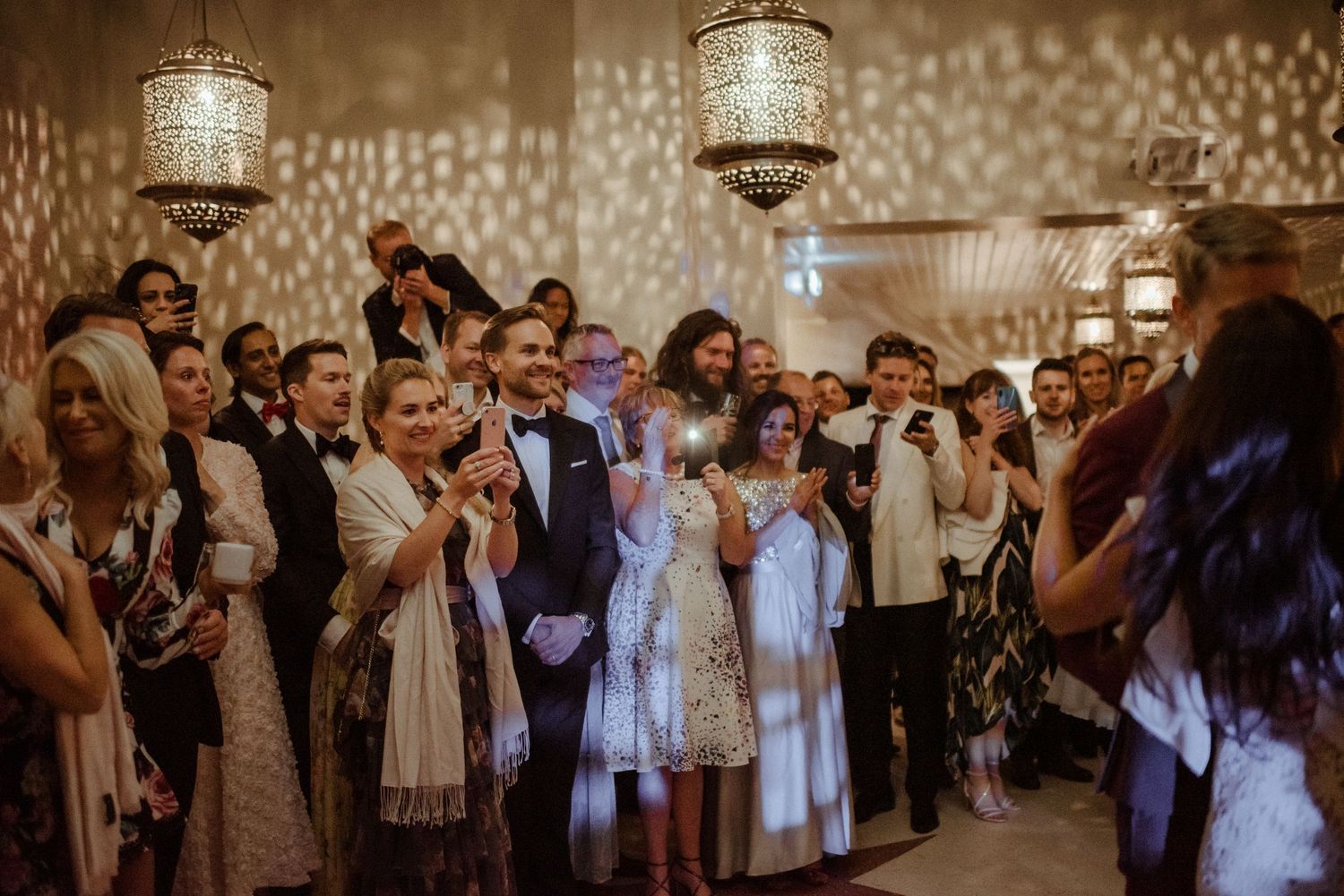 Wedding reception guests gather under crystal chandeliers while celebrating on the dance floor.