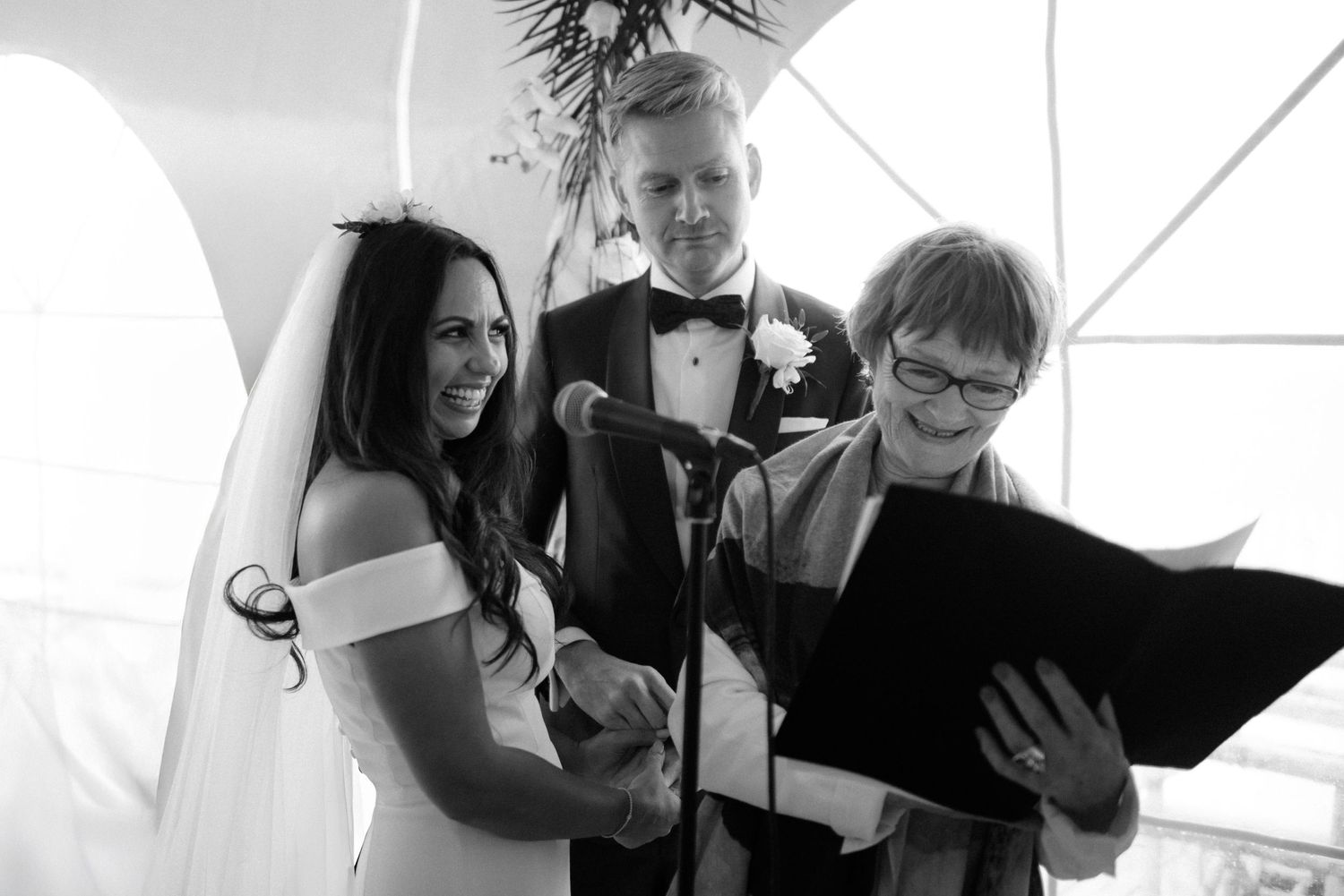 A black and white photo capturing a joyful wedding ceremony moment with a bride, groom and officiant at the altar at Villa Malla in Norway.