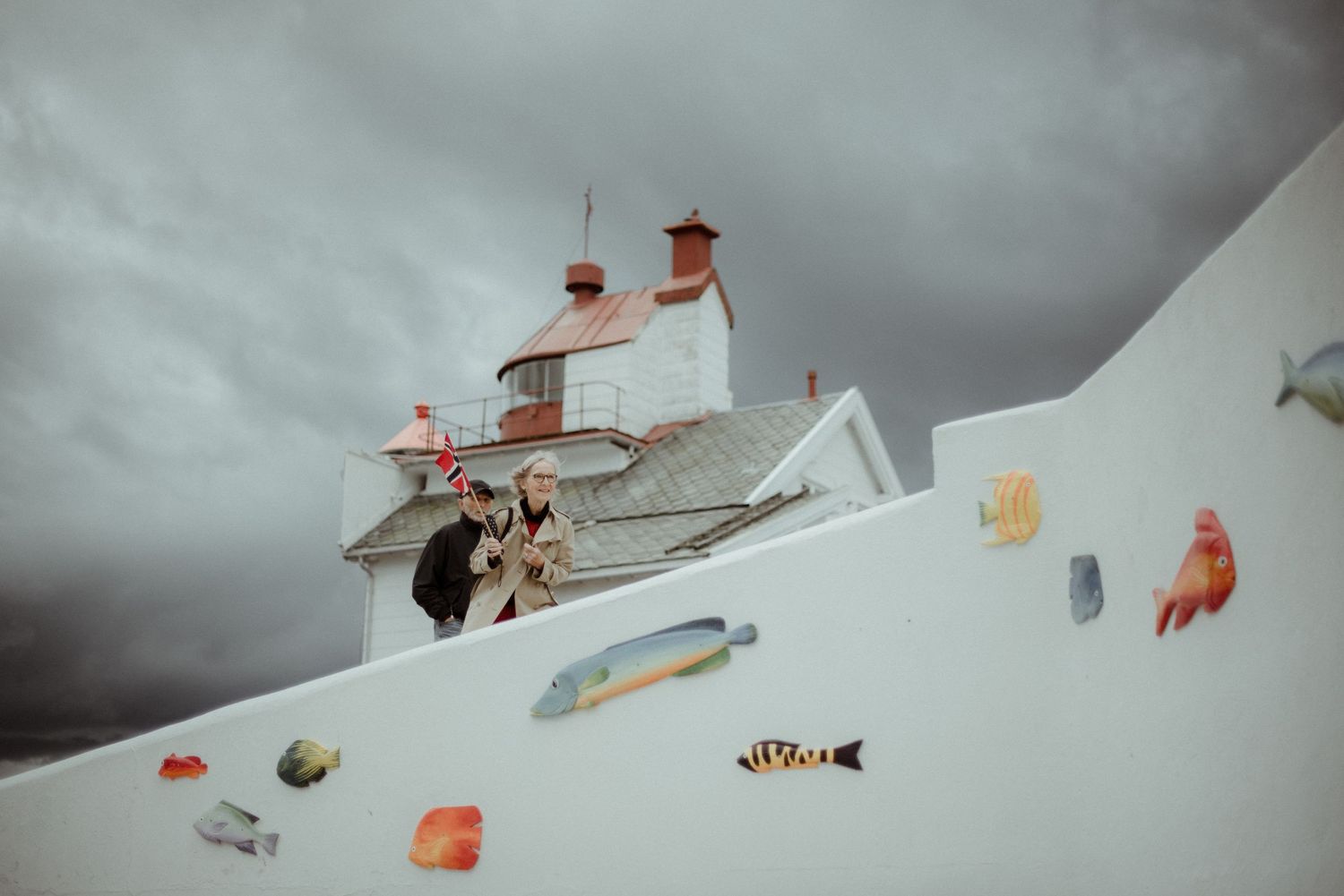 A lighthouse-style white building with fish and sea creature illustrations painted on its sloping wall against a moody sky at Villa Malla.