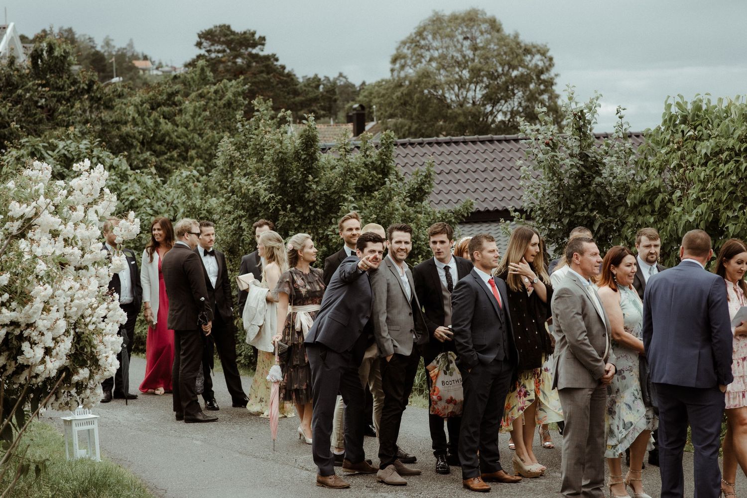 A group of wedding guests gather outside in formal attire during an outdoor garden reception at Villa Malla in Norway.
