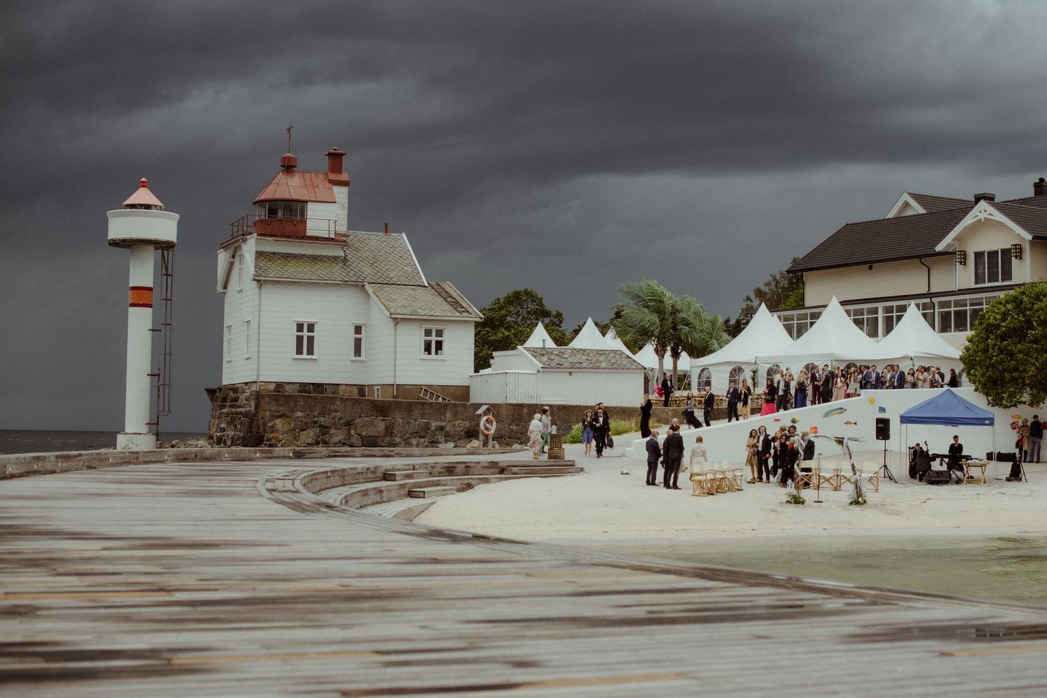 White lighthouse and tents at a waterfront market under stormy skies at Villa Malla in Norway.