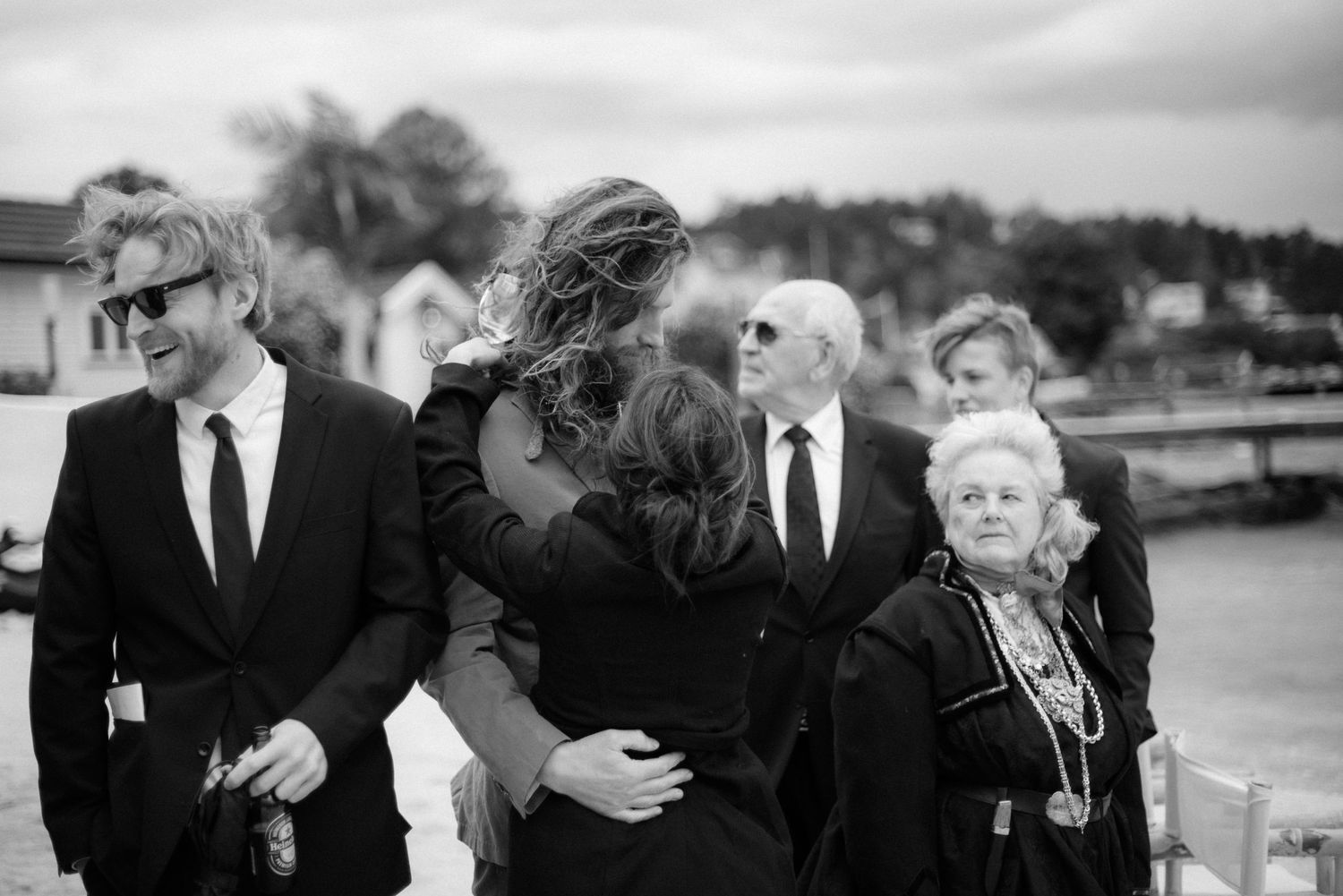 A group of formally dressed people gather near a waterfront in black and white at Villa Malla in Norway.