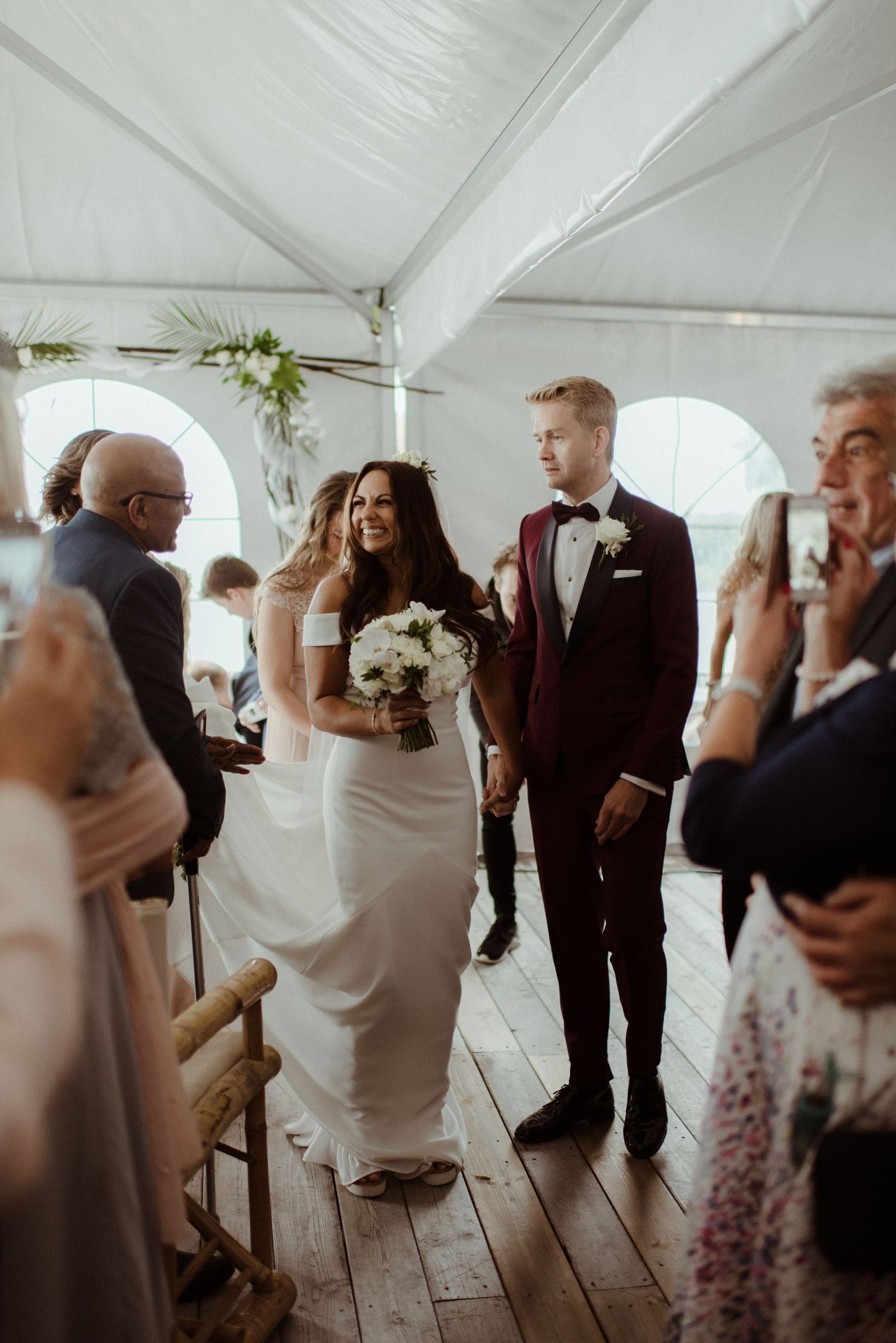 A couple celebrates during their wedding ceremony under a white tent decorated with floral arrangements at Villa Malla in Norway.