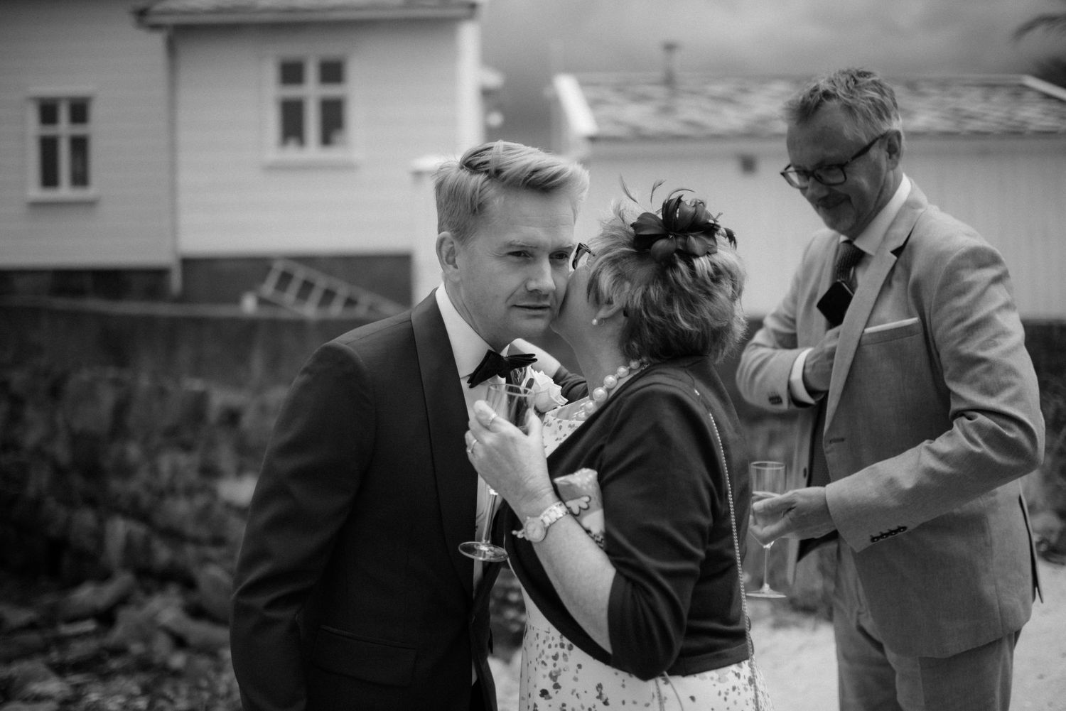 A black and white photograph showing people conversing outdoors near a white house at Villa Malla in Norway.