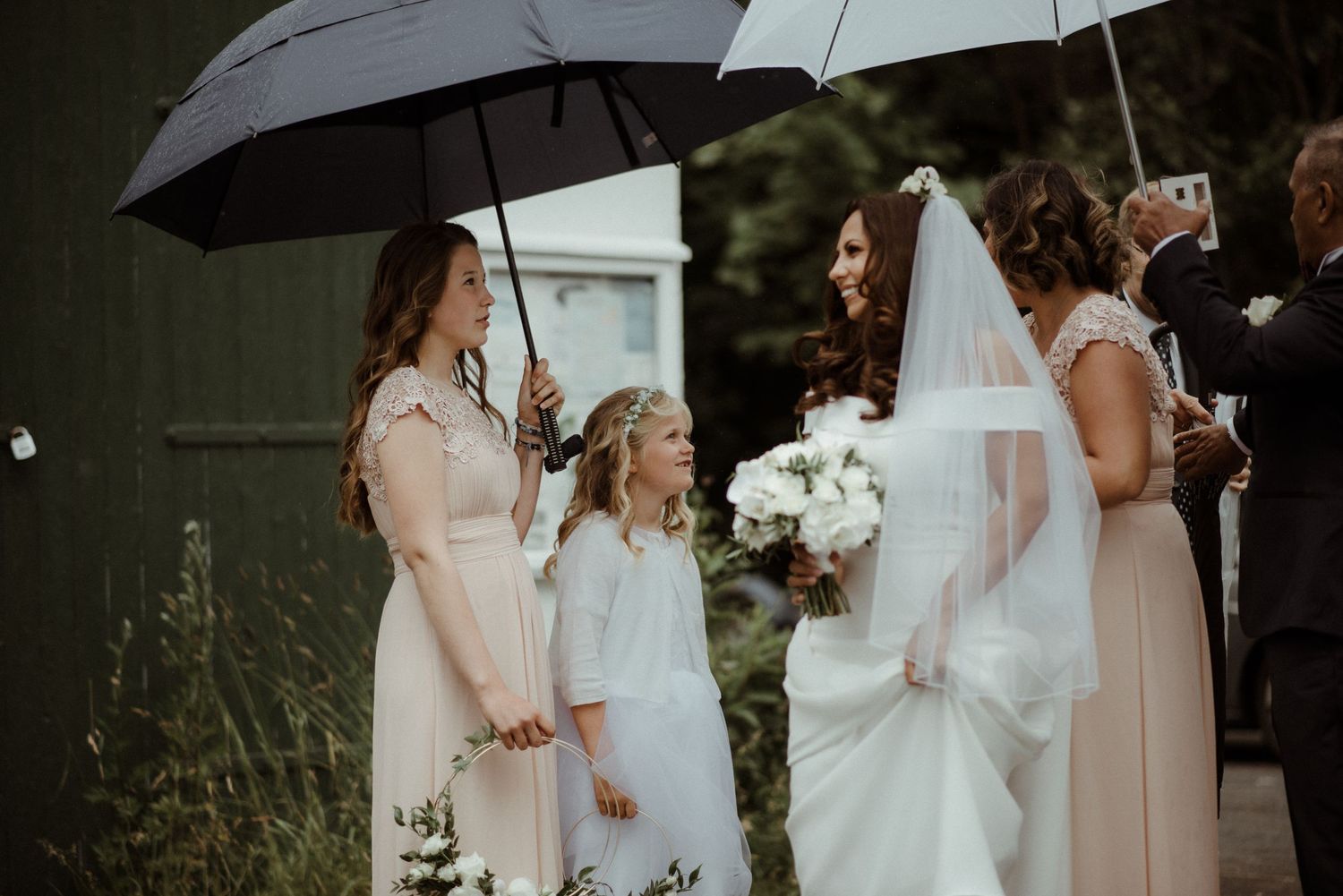 Wedding party members hold umbrellas while gathering outdoors in light rain at Villa Malla in Norway.