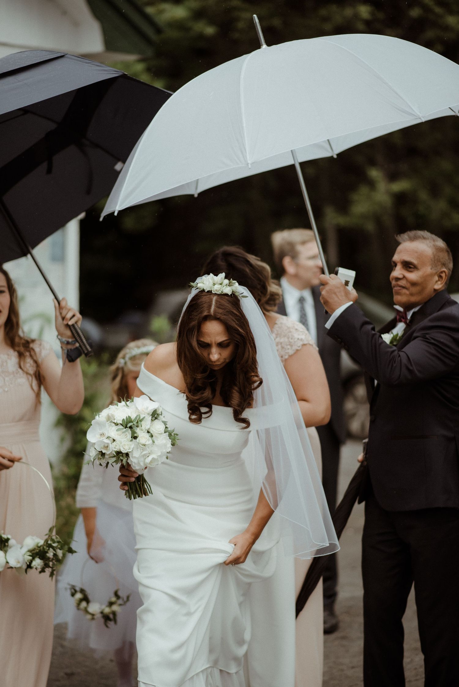 Wedding party stands under black and white umbrellas while bride in white dress holds bouquet of white flowers at Villa Malla in Norway.