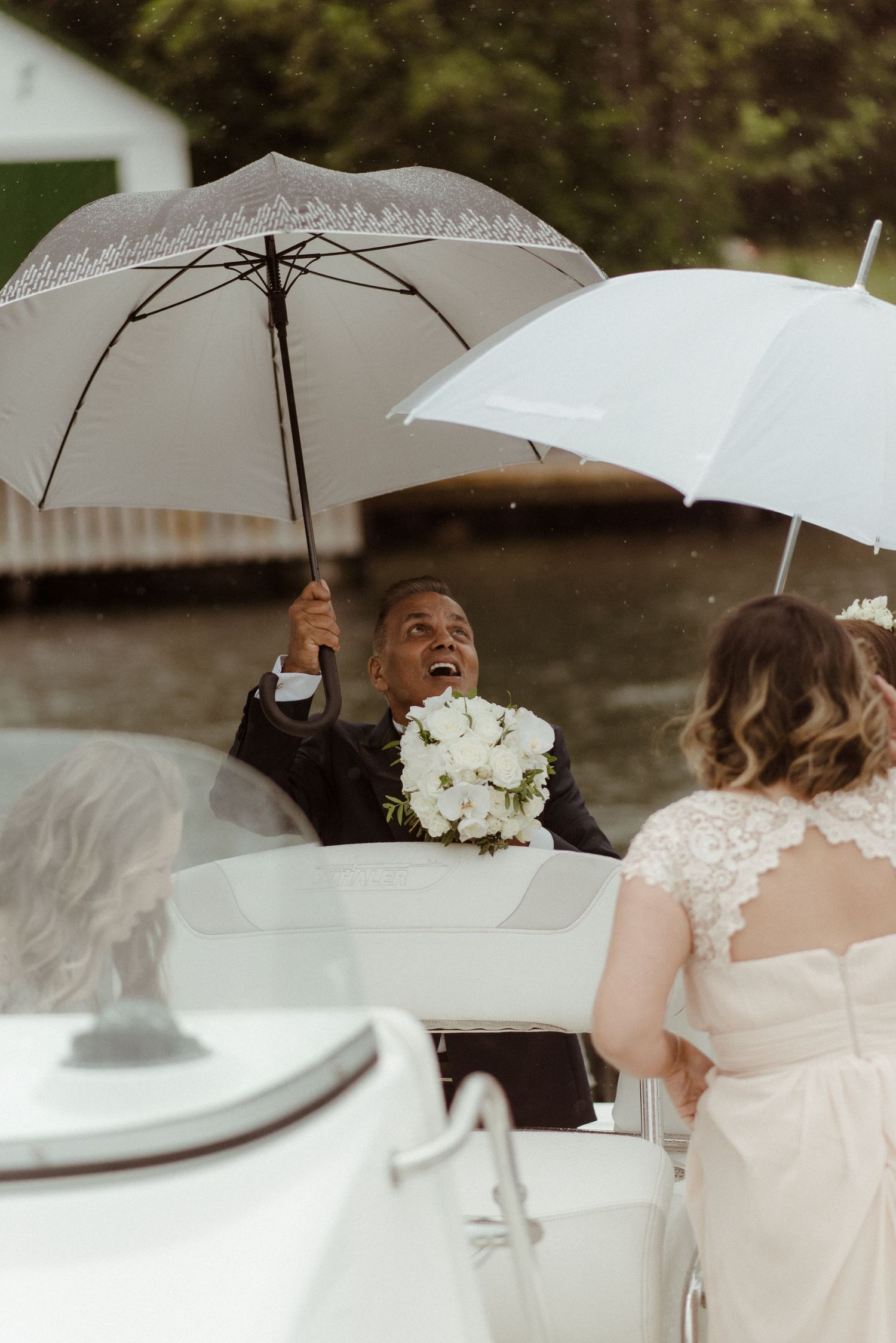Wedding party holding umbrellas on a boat while holding white flower bouquets during a rainy celebration at Villa Malla in Norway.
