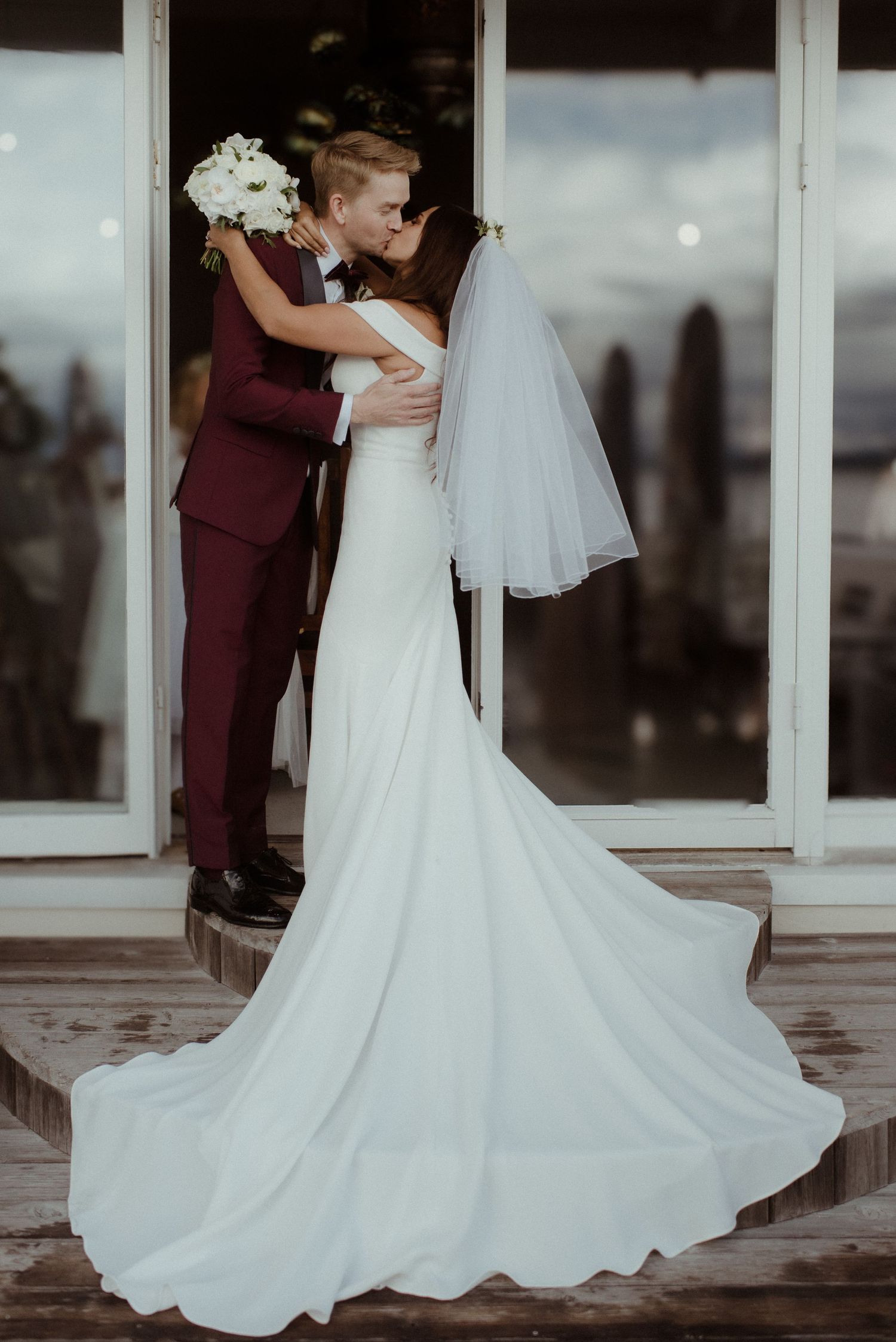 A couple shares a romantic moment at their wedding, with the bride wearing a flowing white gown and the groom in burgundy at Villa Malla.
