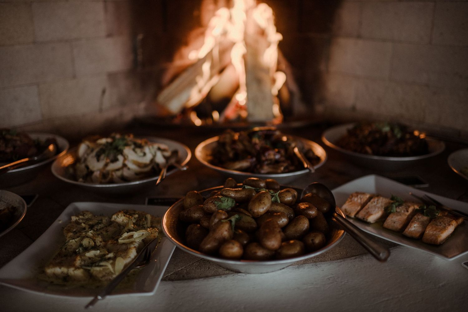 Rustic feast spread with multiple dishes served in earthenware bowls near a glowing fireplace at Villa Malla in Norway.
