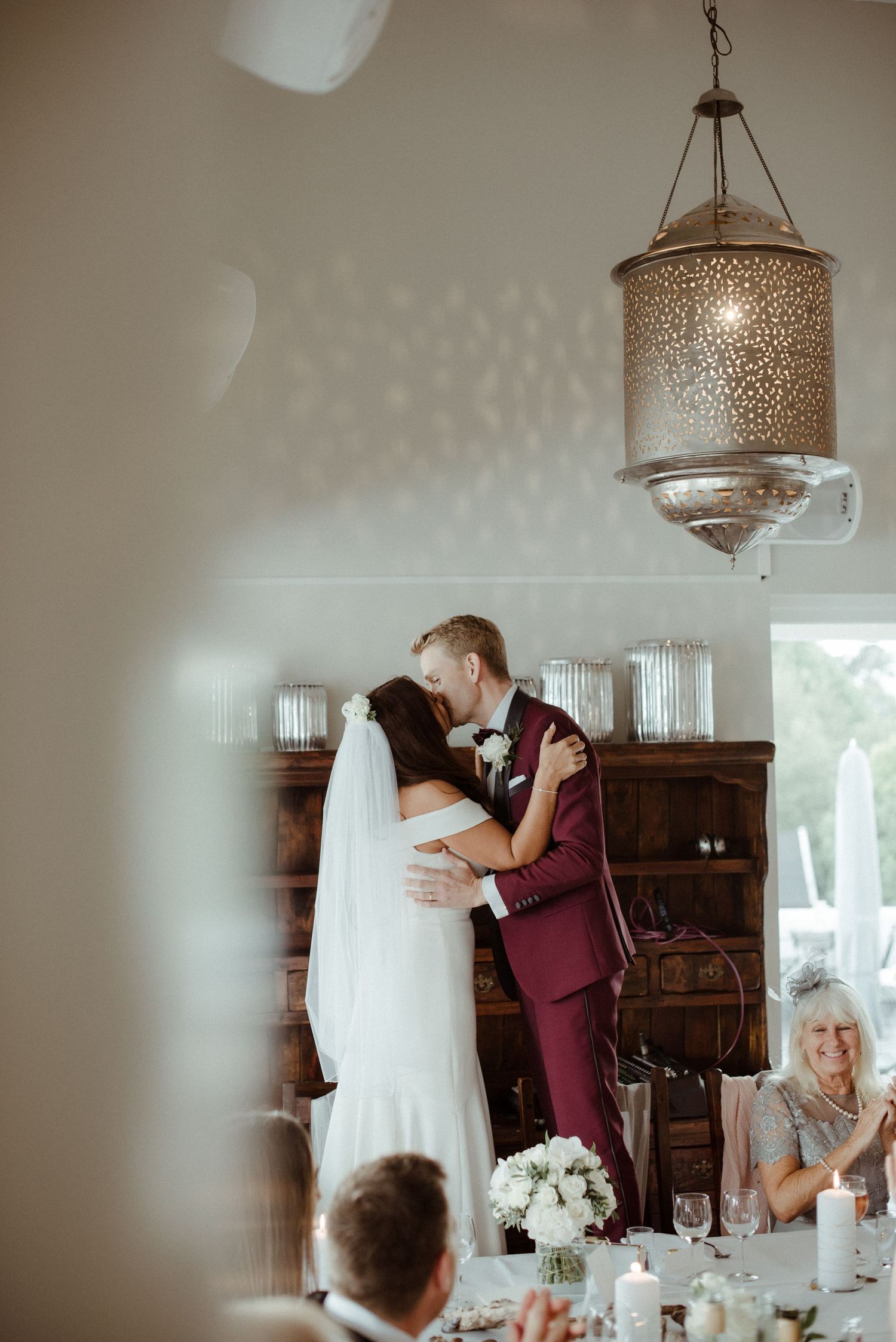 Elegant wedding reception scene with couple kissing under while guests look on from decorated dining tables at Villa Malla in Norway.