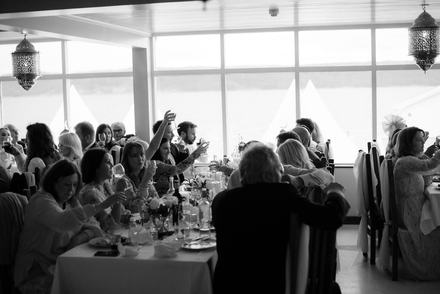 Black and white photo of wedding reception guests dining at tables with elegant hanging lanterns decorating the venue at Villa Malla.