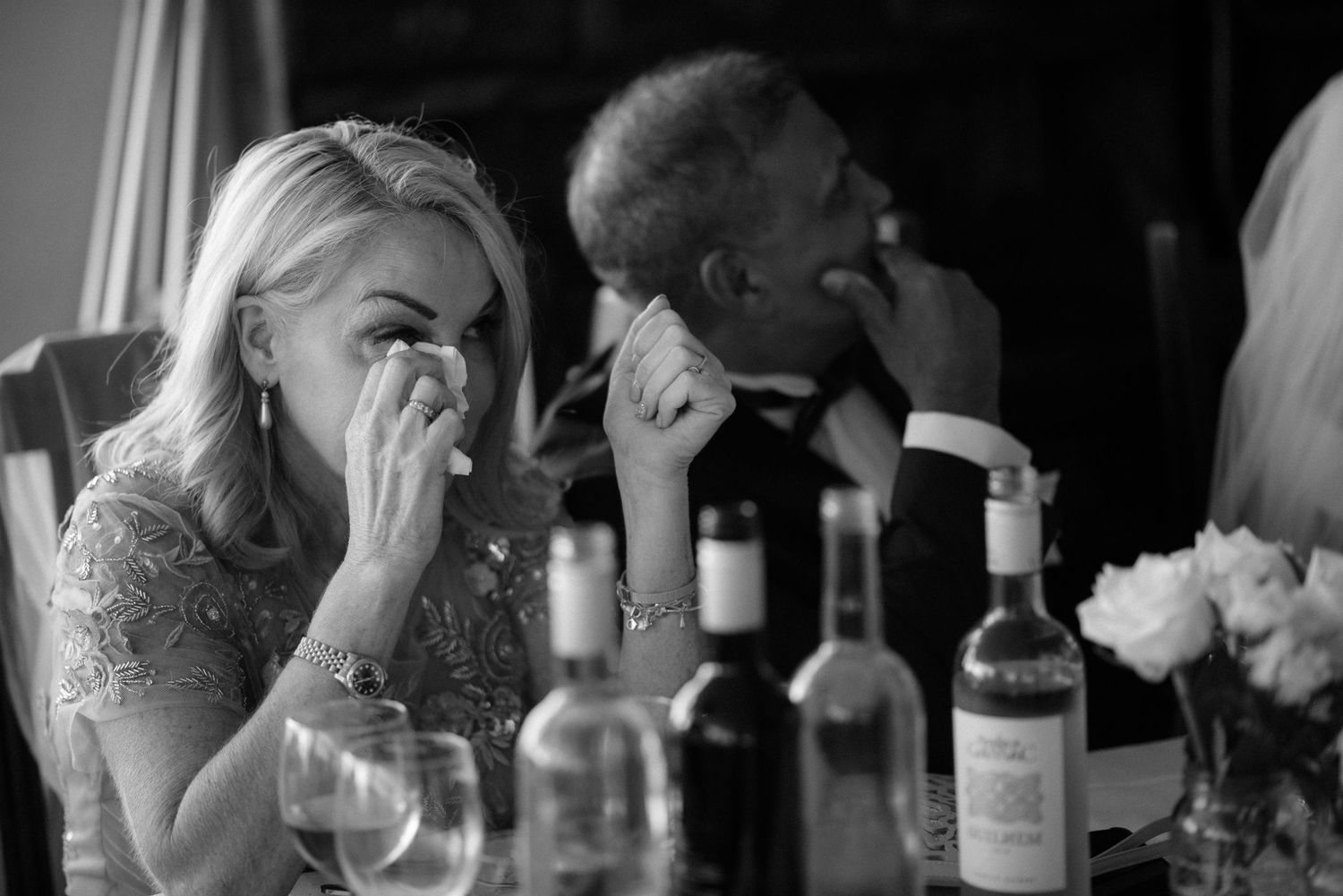 Black and white candid photo of diners showing emotion at an elegant dinner party with wine bottles on the table at Villa Malla in Filtvet,