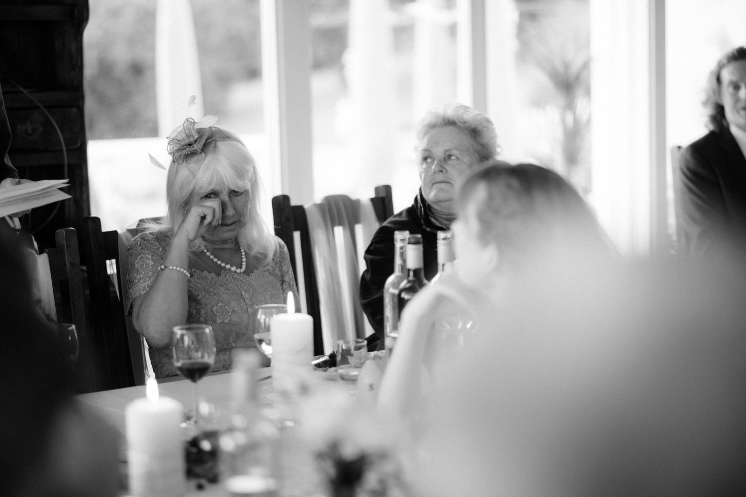 A candid black and white photo shows people seated at a dining table engaged in conversation at Villa Malla in Filtvet, Norway.
