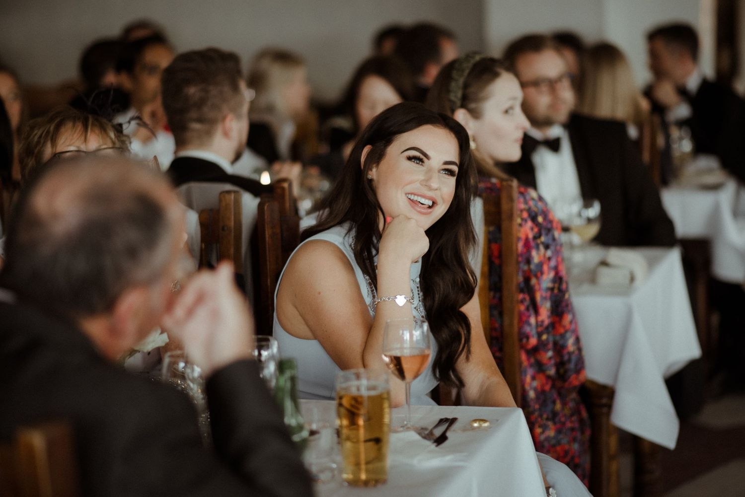 A guest at an elegant wedding reception smiles while seated at a white-clothed table during dinner at Villa Malla in Filtvet, Norway.