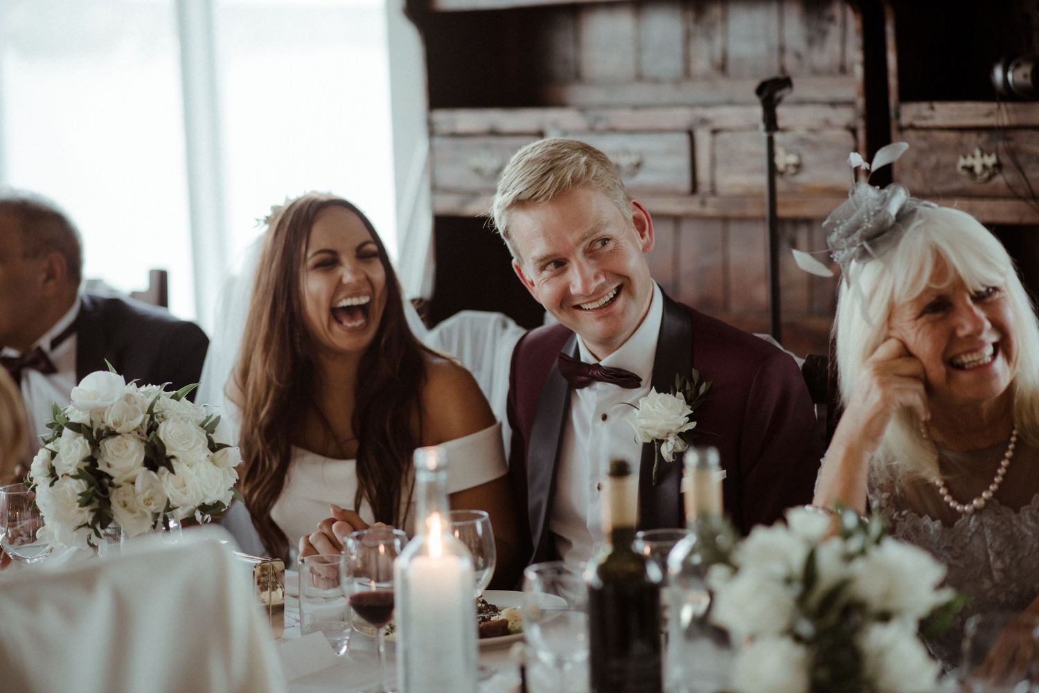 Wedding reception guests sharing a candid moment of laughter at an elegantly decorated dinner table at Villa Malla in Filtvet, Norway.