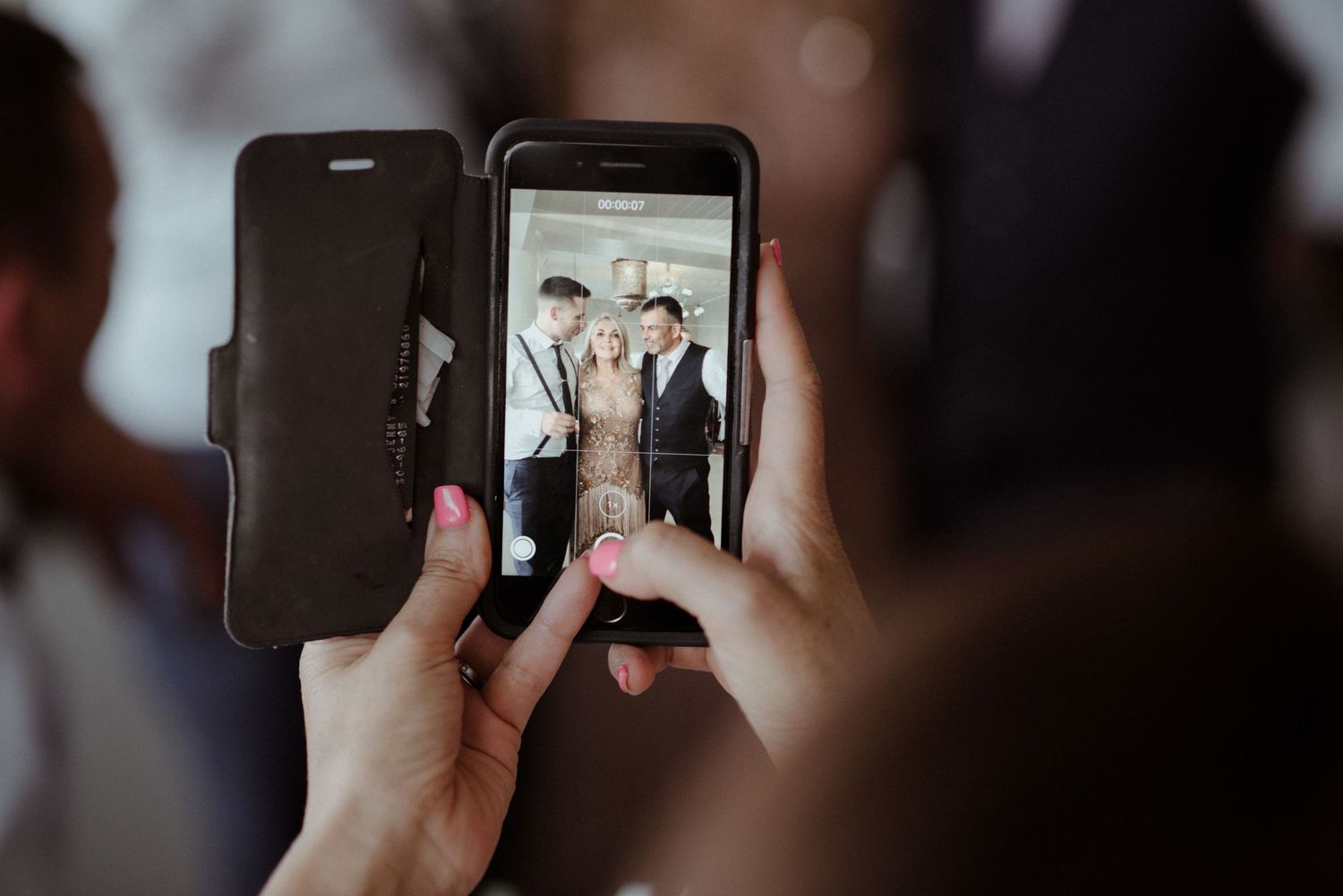Close up view of hands holding smartphone taking photos at a wedding t through black folio case at Villa Malla in Filtvet, Norway.