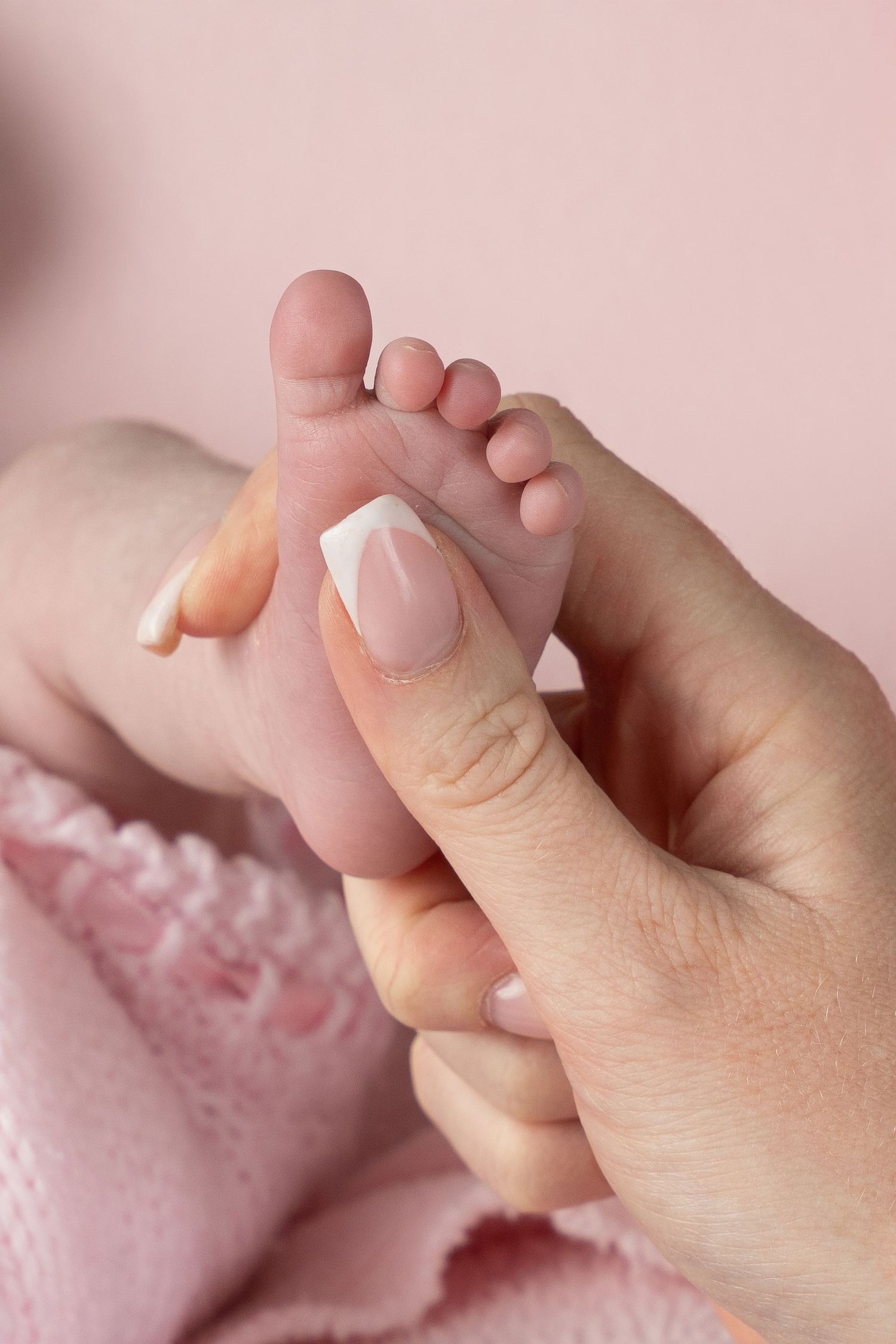 Gentle massage of tiny baby toes against pink background showing tender newborn care.
