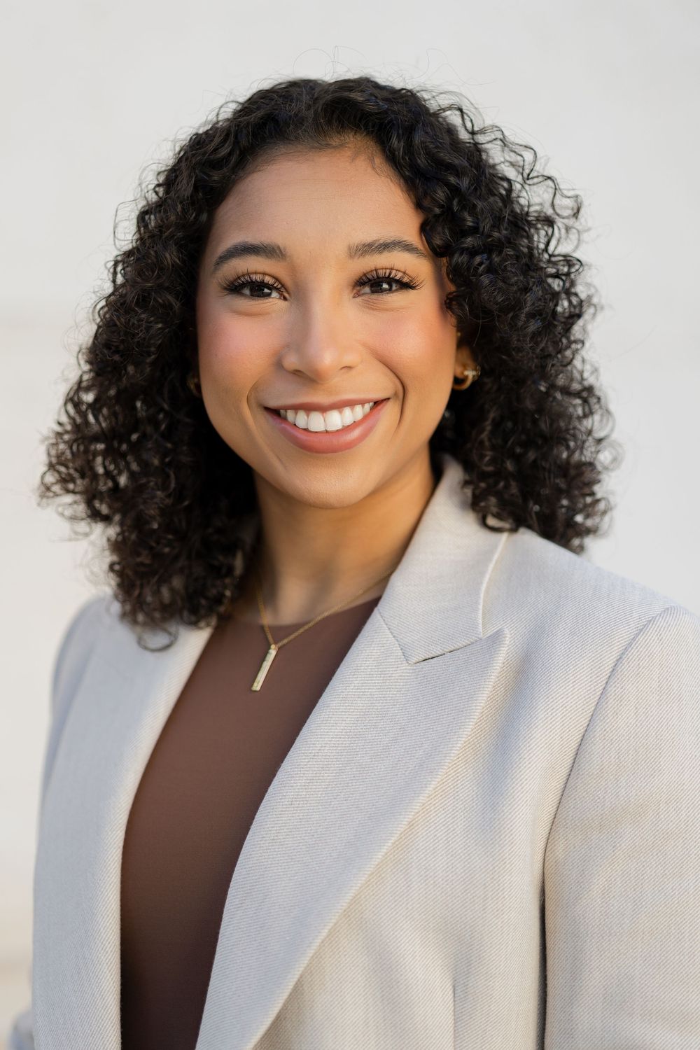 Professional headshot of woman in cream blazer and brown top against white background.