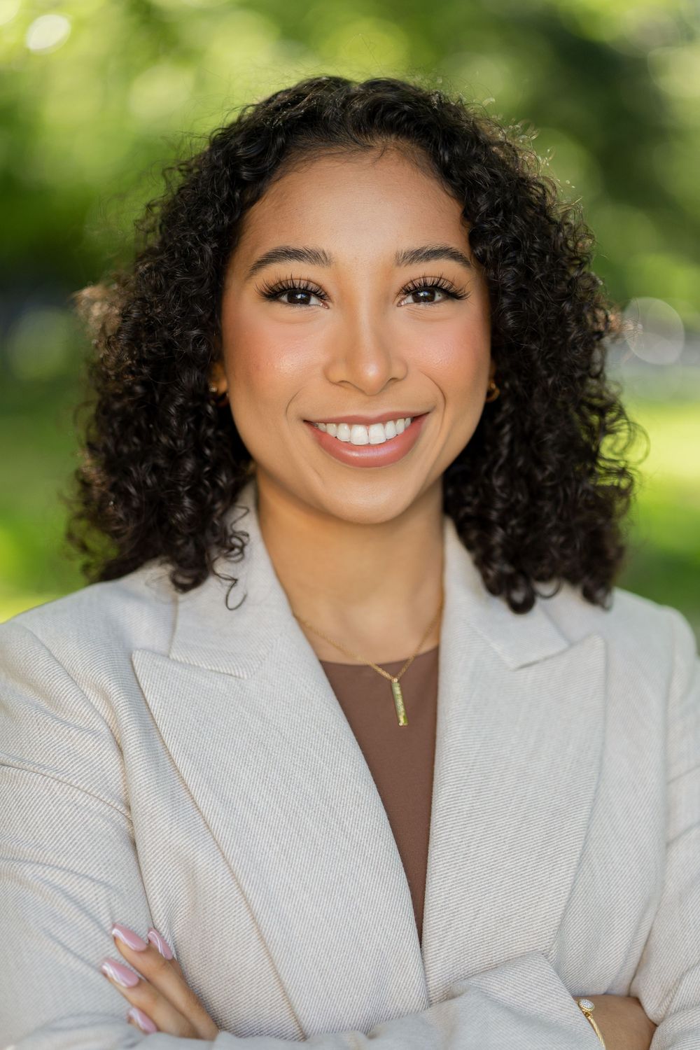 Professional portrait of woman in cream blazer smiling against blurred green background.