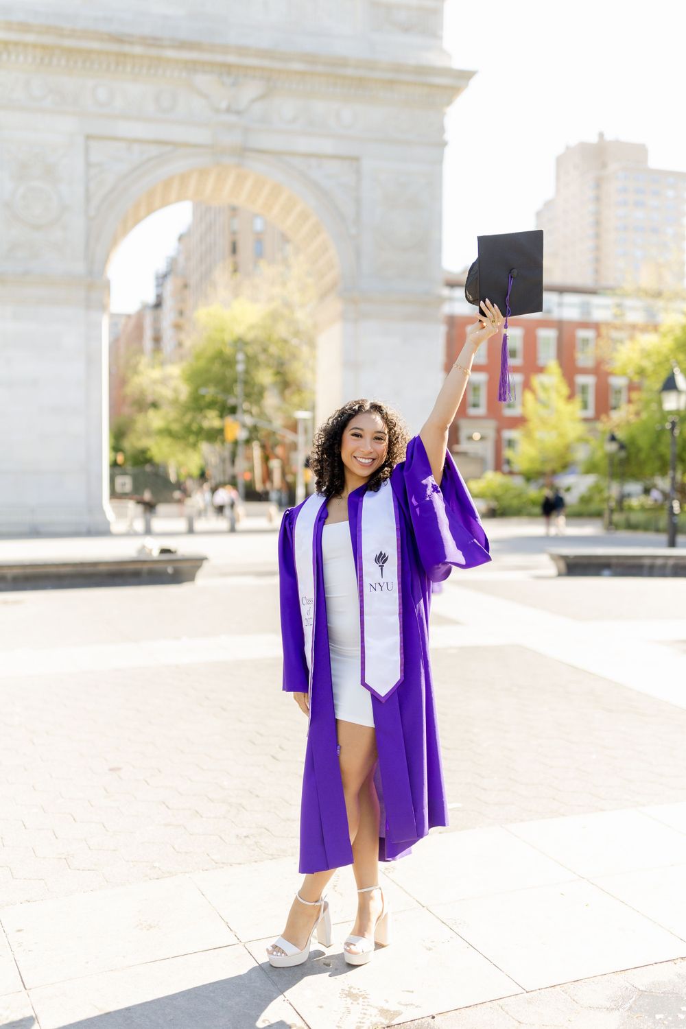 Graduate celebrates with cap raised high in front of iconic Washington Square Arch.